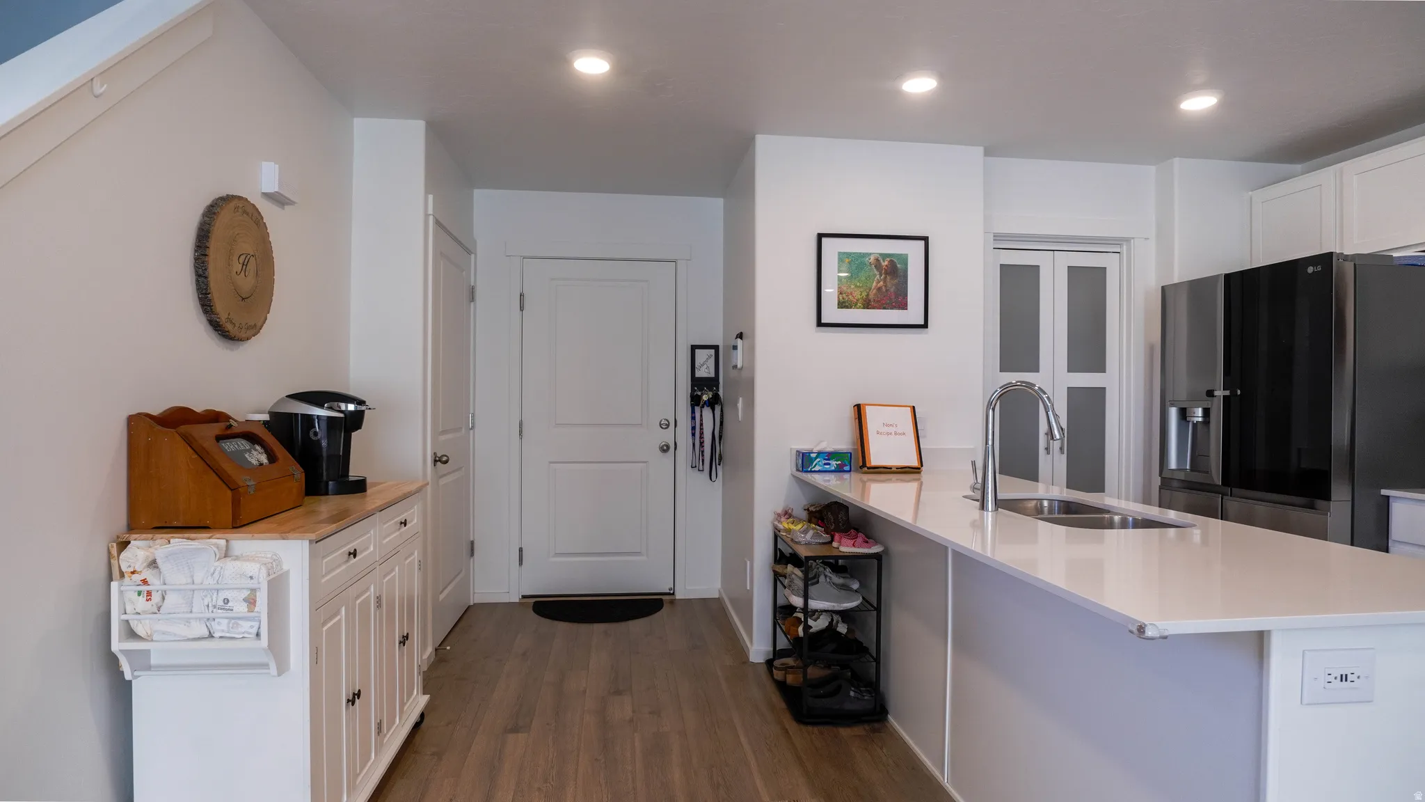 Kitchen with white cabinetry, stainless steel fridge, a peninsula, dark wood finished floors, and a kitchen bar