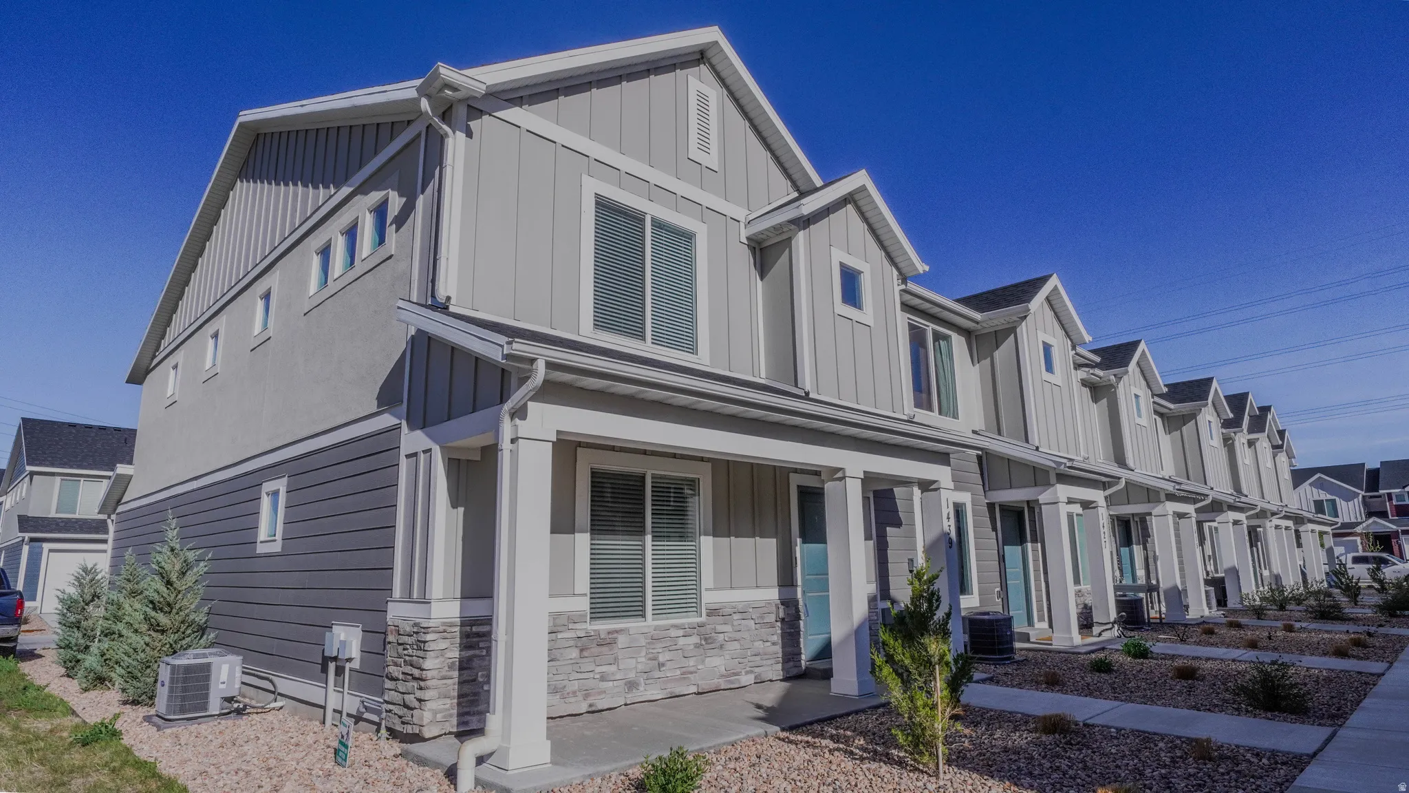 Modern townhome exterior featuring light gray vertical siding, dark gray horizontal siding, and stone veneer accents