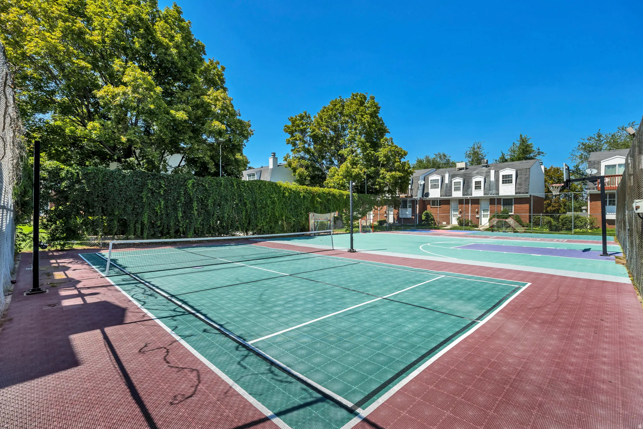 Multi-sport court featuring a tennis court with net, a basketball hoop, and a perimeter fence.