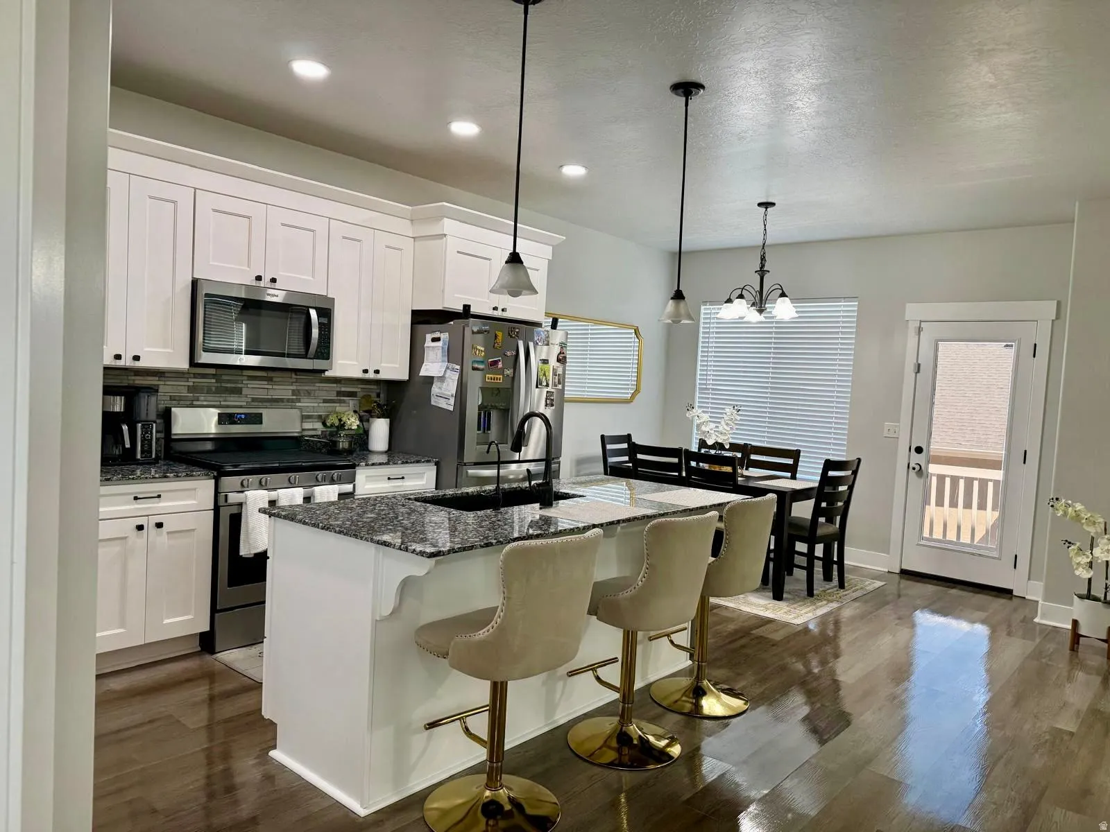 Kitchen featuring stainless steel appliances, dark stone countertops, decorative backsplash, dark wood-style flooring, and a textured ceiling