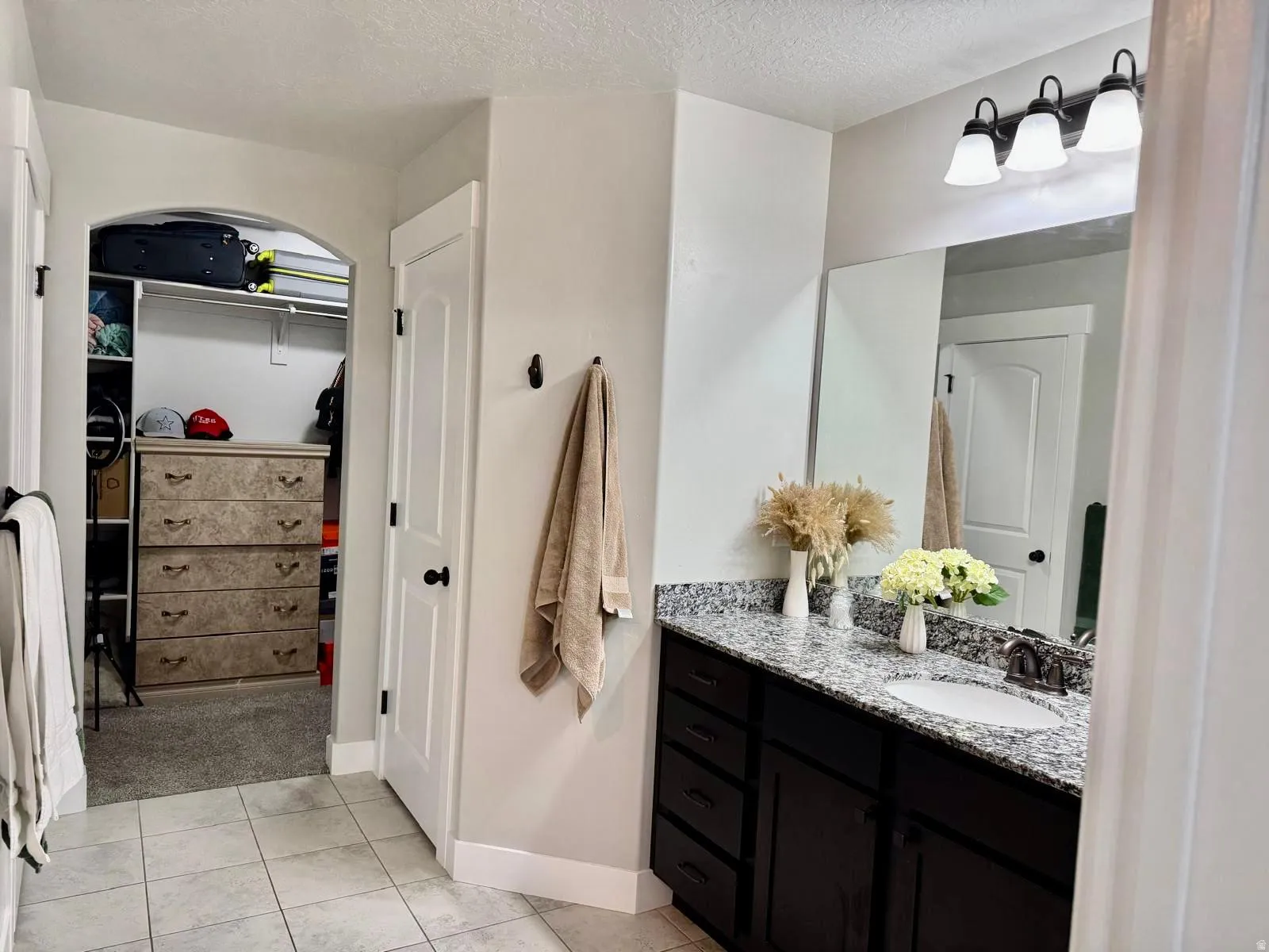 Full bath with a spacious closet, vanity, a textured ceiling, and light tile patterned floors