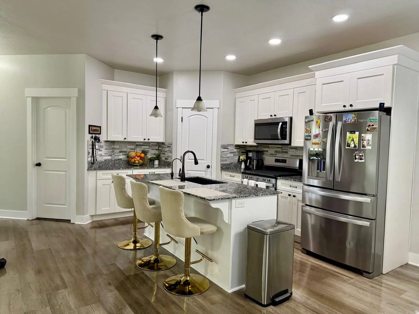 Kitchen featuring stainless steel appliances, a breakfast bar, dark stone counters, white cabinets, and a kitchen island with sink