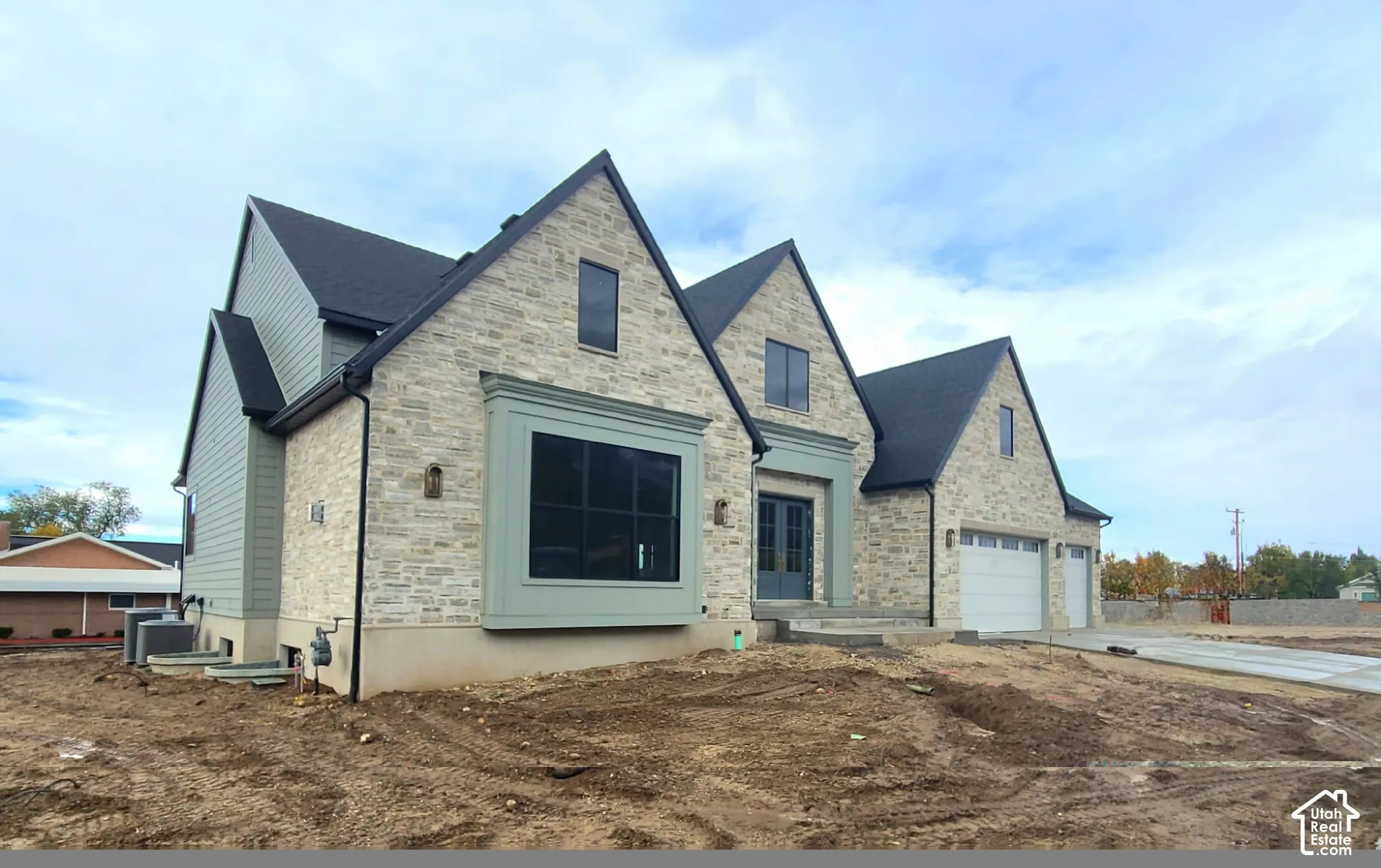 Multi-gabled exterior featuring light stone masonry, green lap siding, a box bay window, and a three-car garage