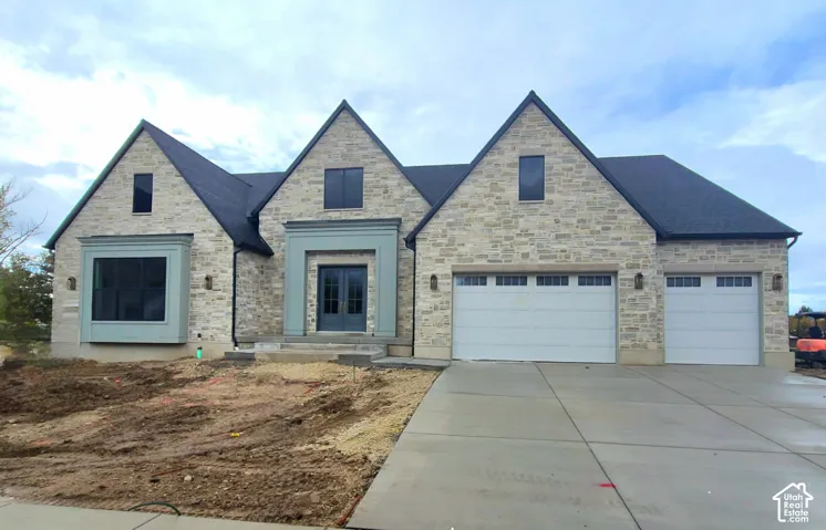 Multi-gabled exterior featuring natural stone facade, dark shingle roof, double-entry front doors, bay window, and a three-car garage