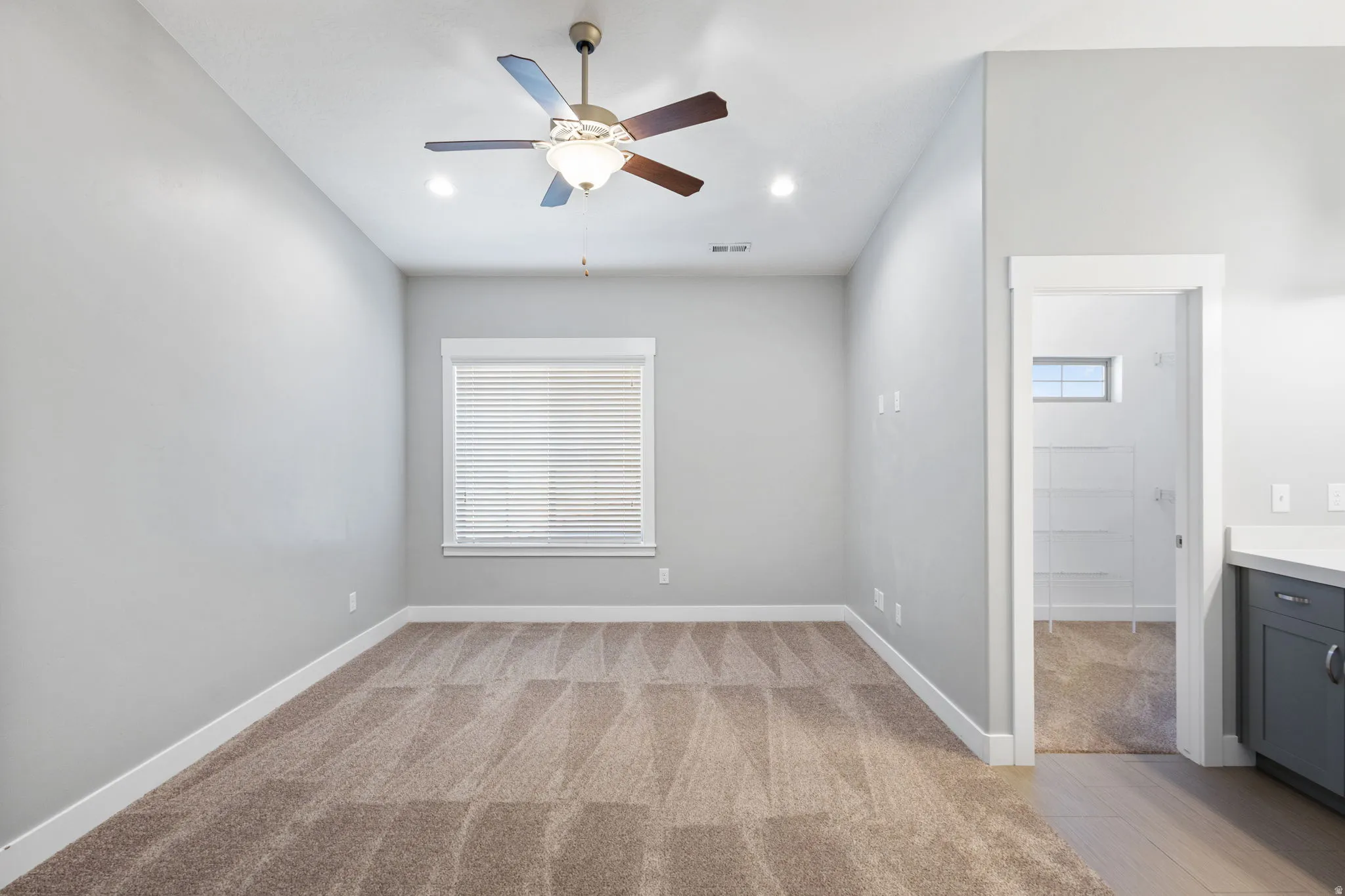 Empty room featuring ceiling fan, light colored carpet, and healthy amount of natural light