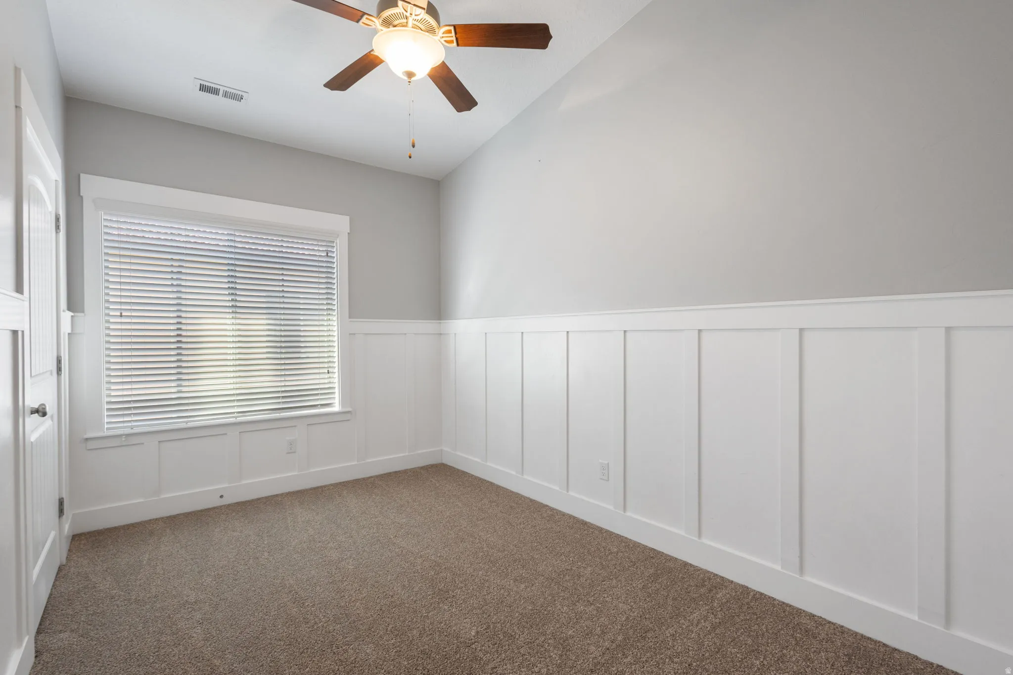 Spare room with wainscoting, a decorative wall, a ceiling fan, lofted ceiling, and dark carpet