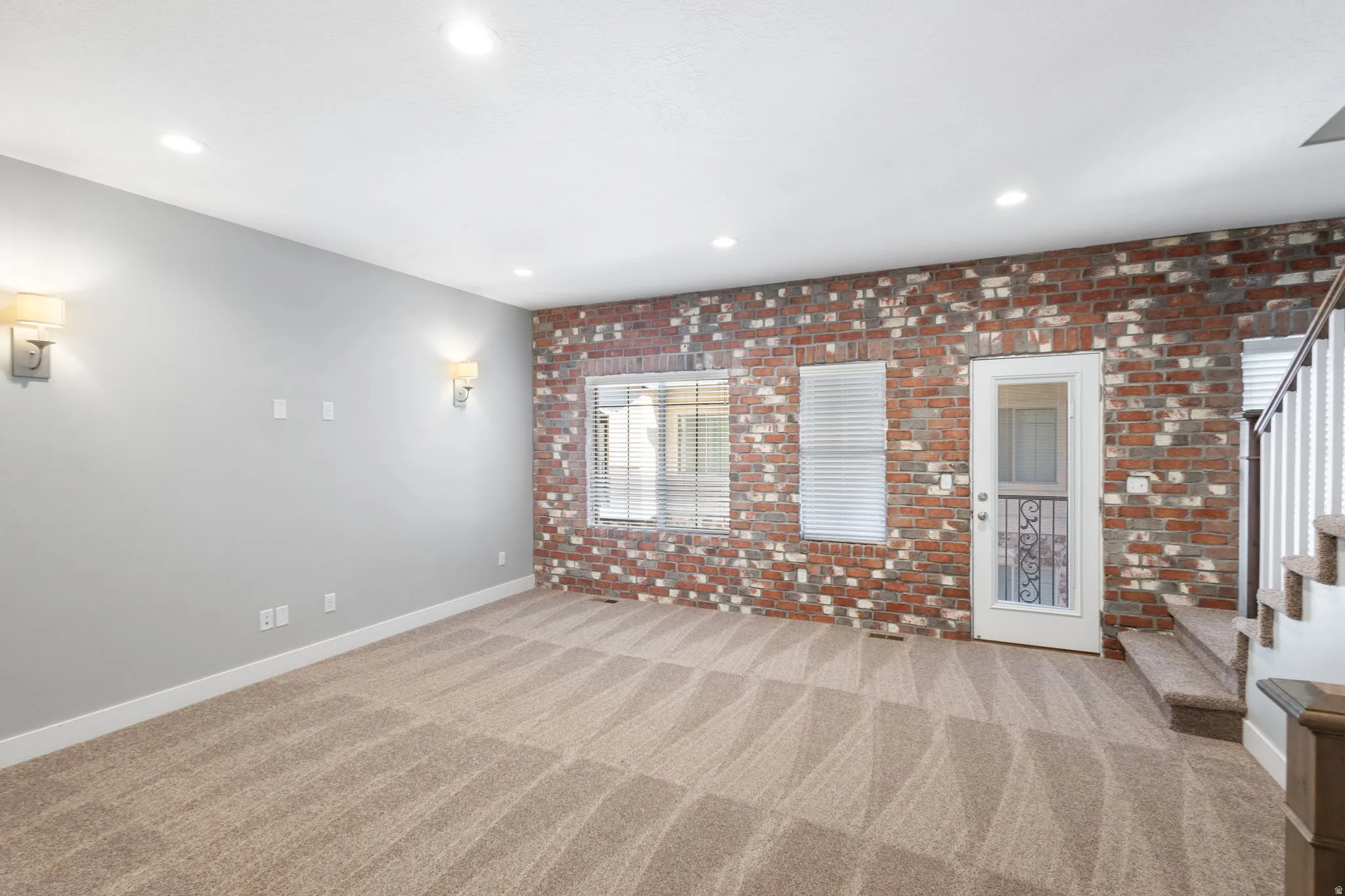 Unfurnished living room with brick wall, light colored carpet, and recessed lighting