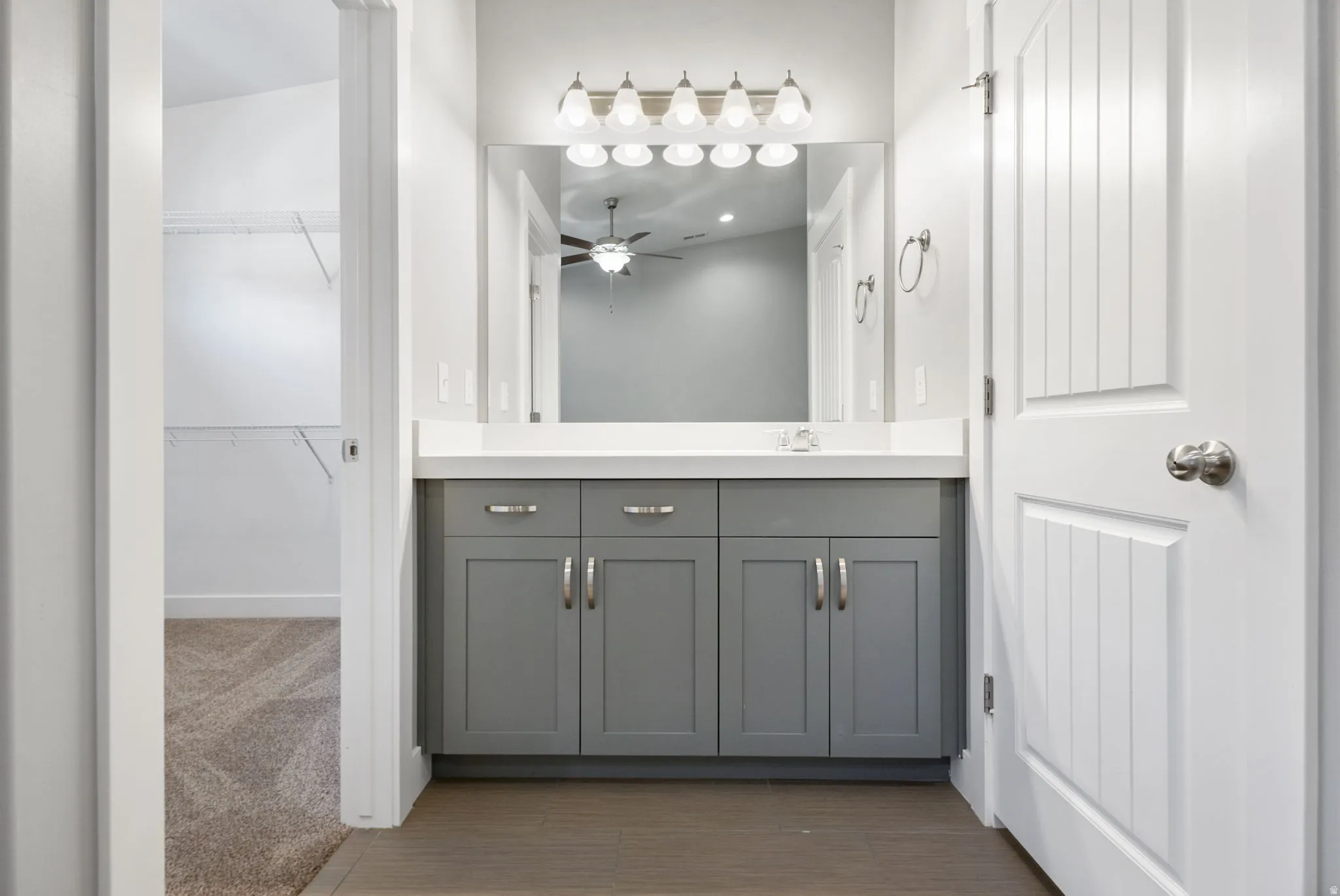 Bathroom with vanity, a walk in closet, a ceiling fan, and dark colored carpet