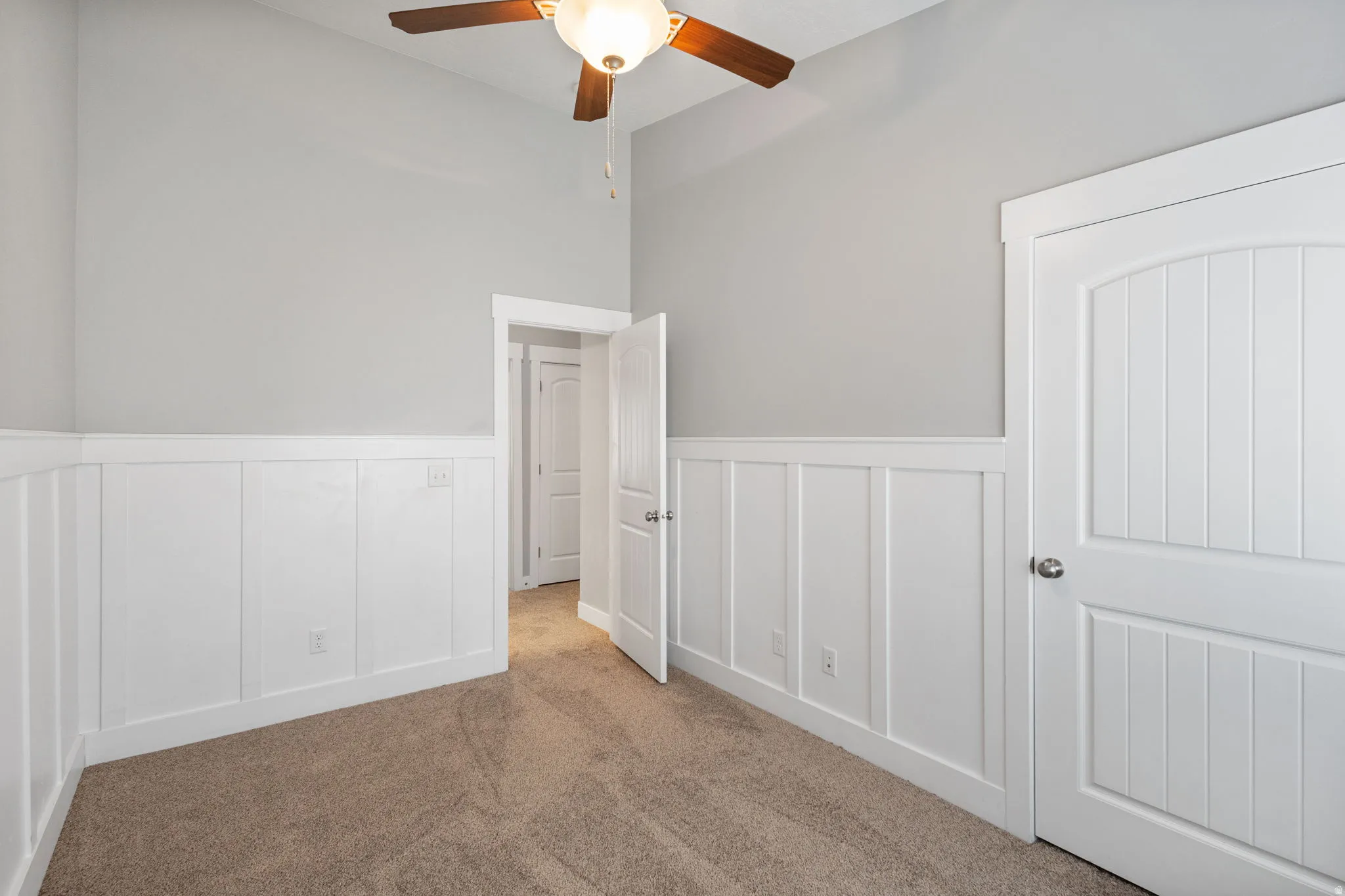 Carpeted spare room with a decorative wall, a wainscoted wall, and a ceiling fan