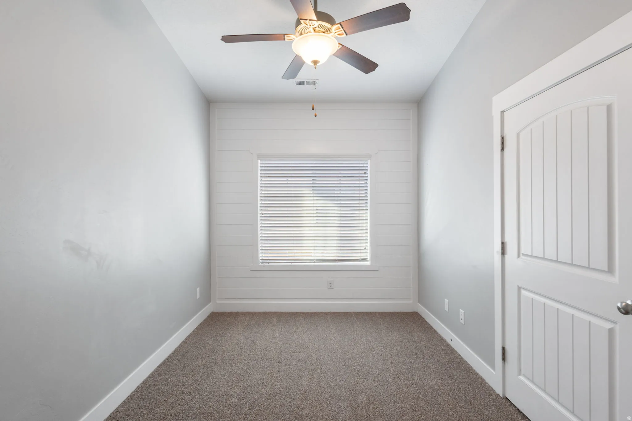 Empty room with a ceiling fan and dark carpet