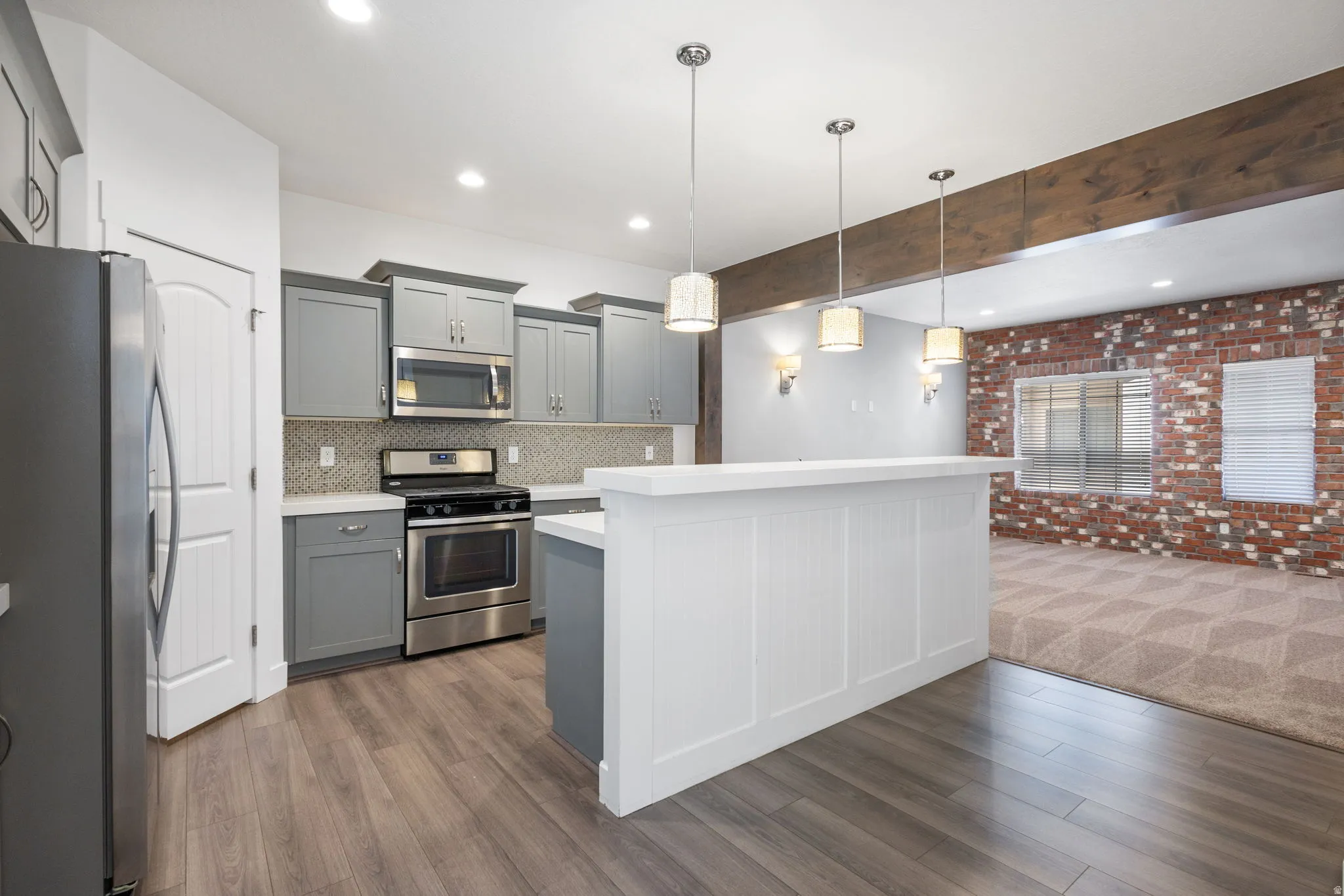 Kitchen with stainless steel appliances, gray cabinetry, light countertops, a center island, and brick wall