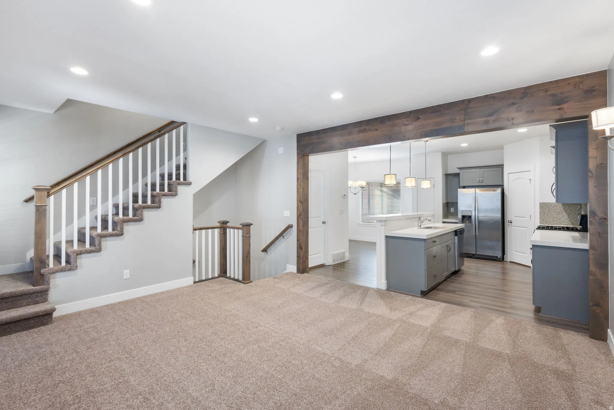 Kitchen featuring an island with sink, hanging light fixtures, dark carpet, gray cabinetry, and stainless steel appliances
