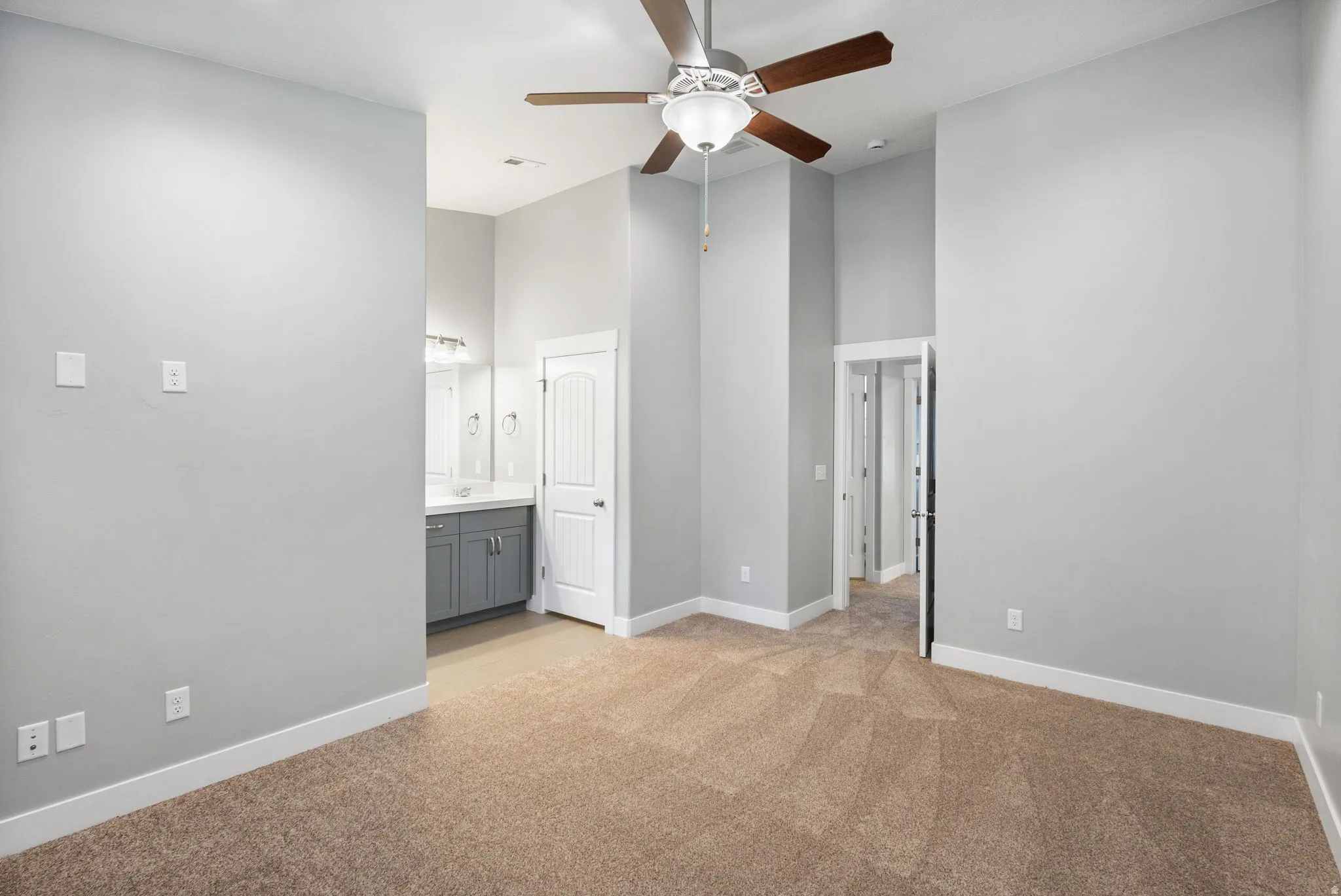 Unfurnished bedroom featuring a high ceiling, light carpet, a ceiling fan, and ensuite bathroom