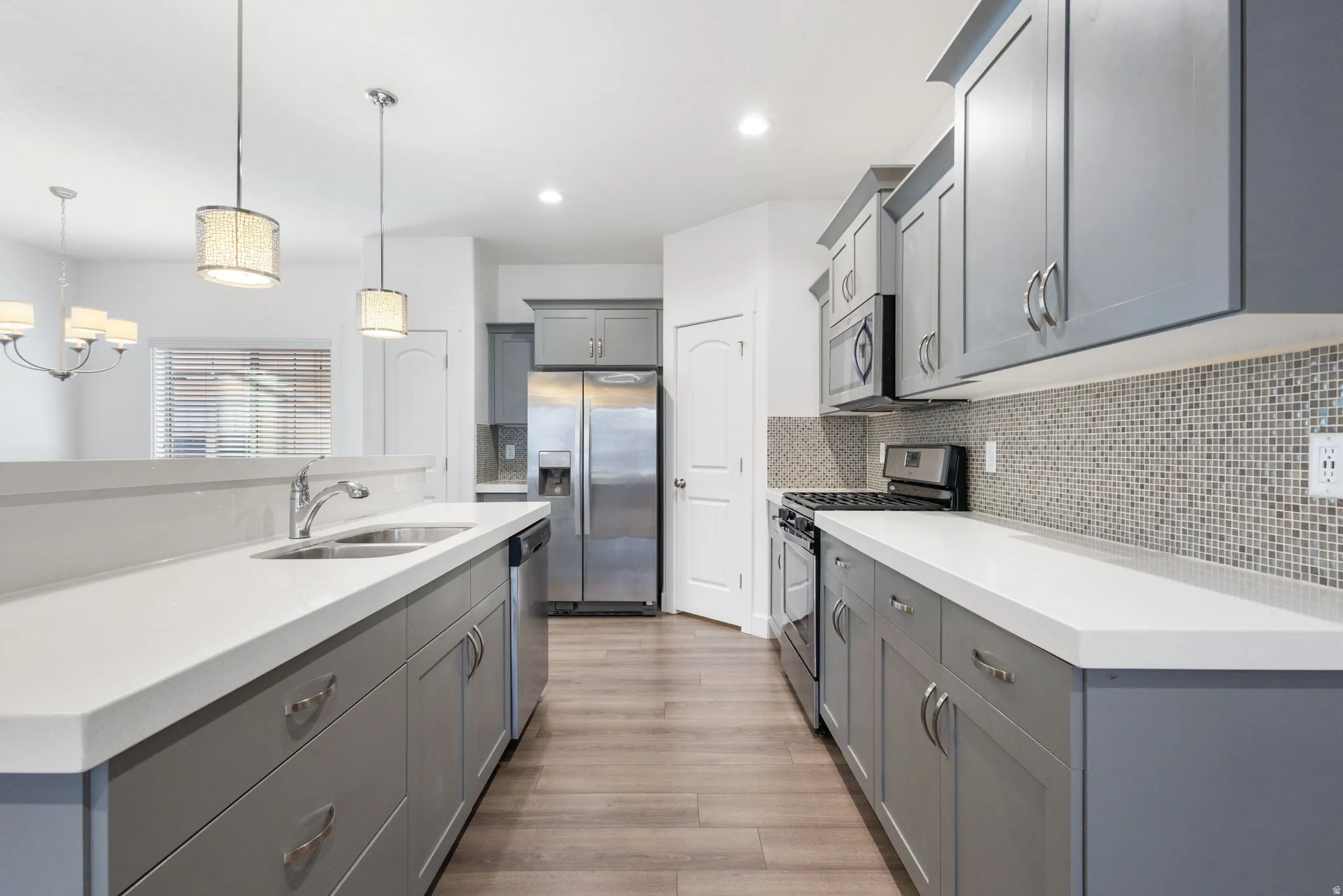 Kitchen featuring gray cabinetry, stainless steel appliances, an island with sink, light wood-style floors, and tasteful backsplash