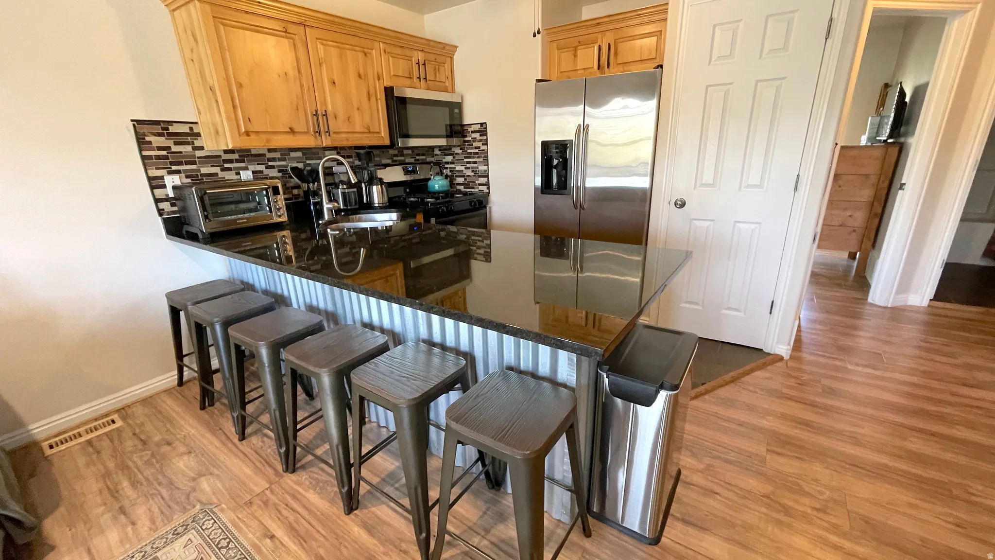 Kitchen featuring a kitchen bar, a peninsula, stainless steel appliances, dark stone counters, and light wood-style floors