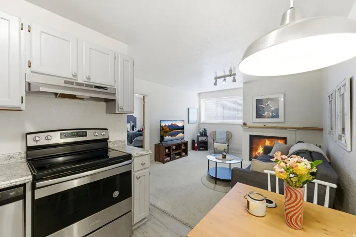 Kitchen featuring stainless steel appliances, light countertops, a glass covered fireplace, open floor plan, and white cabinetry