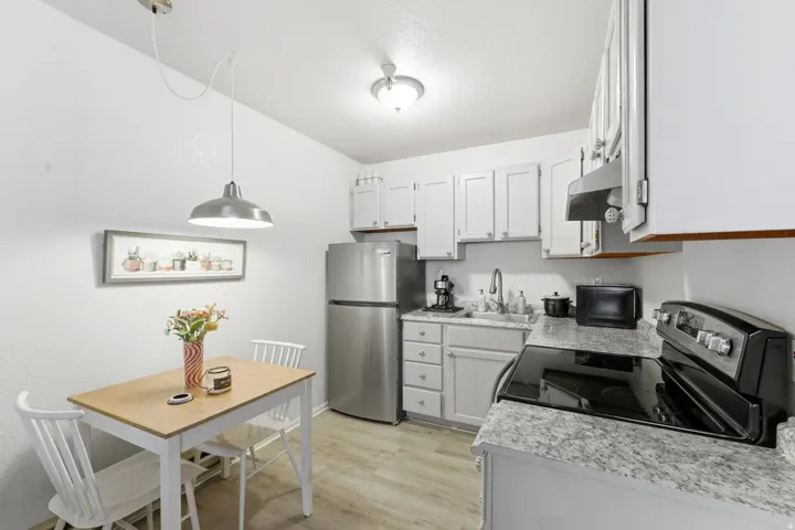 Kitchen with light countertops, stainless steel appliances, light wood-style floors, exhaust hood, and pendant lighting
