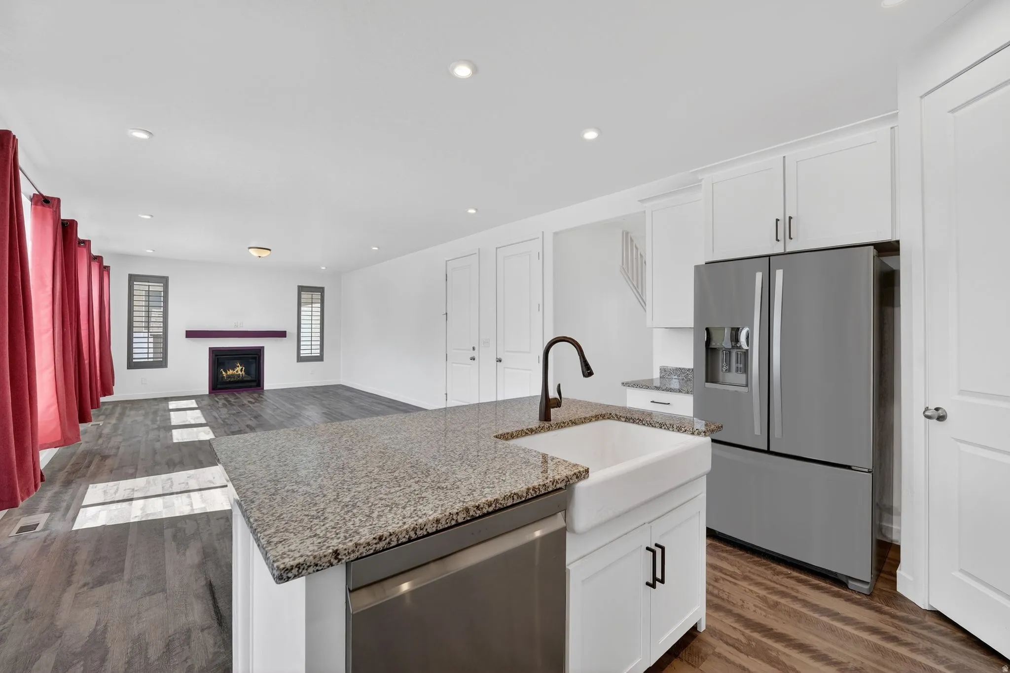 Kitchen featuring dark wood-style floors, stainless steel appliances, a lit fireplace, a kitchen island with sink, and recessed lighting