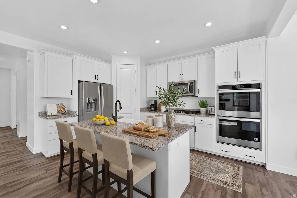 Kitchen featuring stainless steel appliances, a breakfast bar, light stone counters, white cabinetry, and recessed lighting