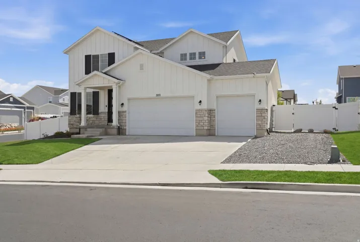 Modern farmhouse style home featuring a gate, a garage, board and batten siding, stone siding, and concrete driveway