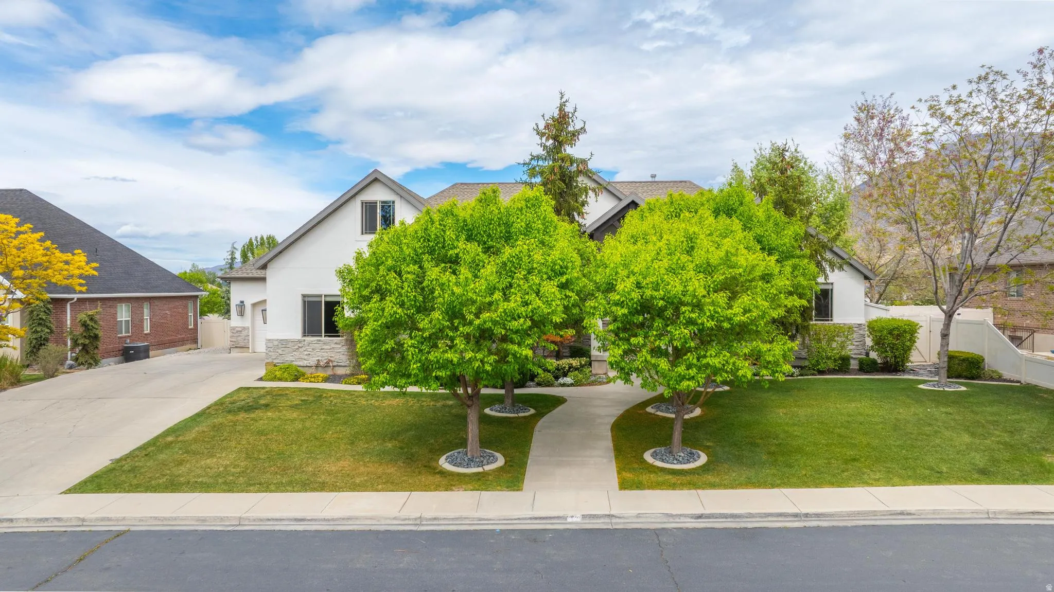View of property hidden behind natural elements with stone siding, stucco siding, and concrete driveway