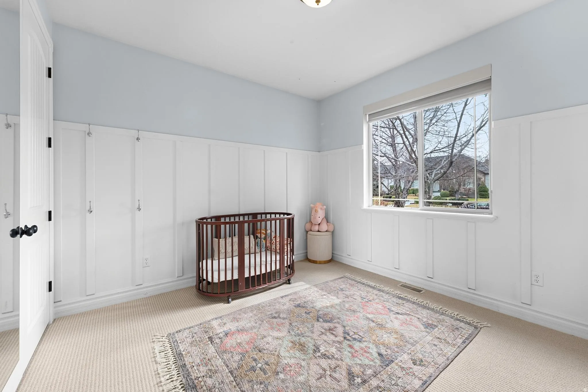 Bedroom with a decorative wall, wainscoting, a crib, and light carpet