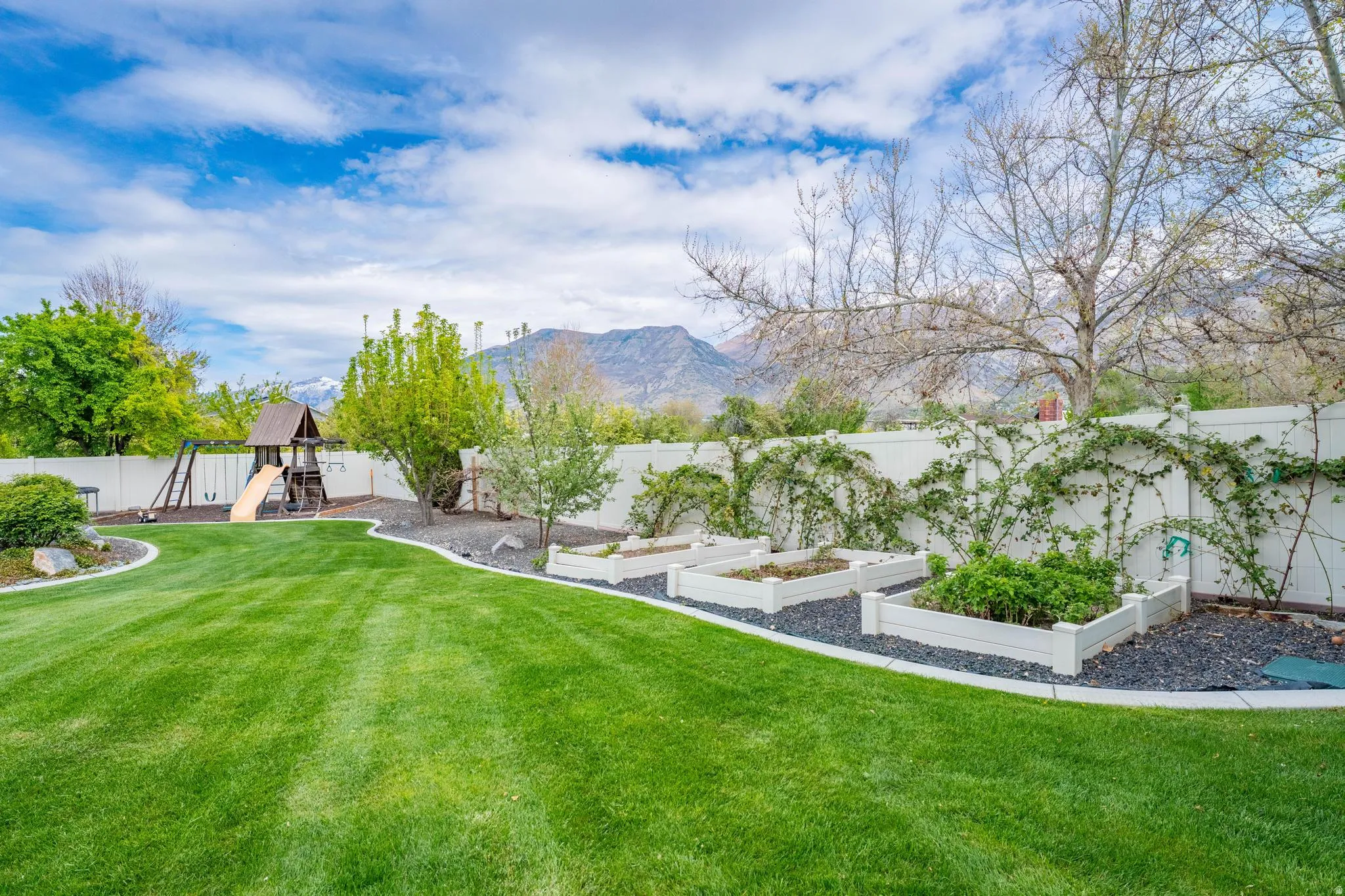 Fenced backyard featuring a vegetable garden, a playground, and a mountain view