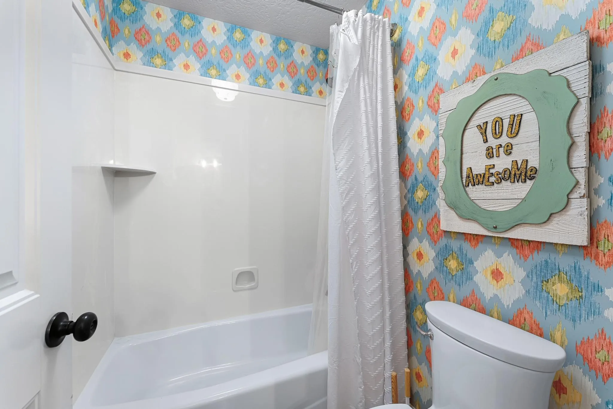 Bathroom with shower / bathtub combination with curtain, wallpapered walls, and a textured ceiling