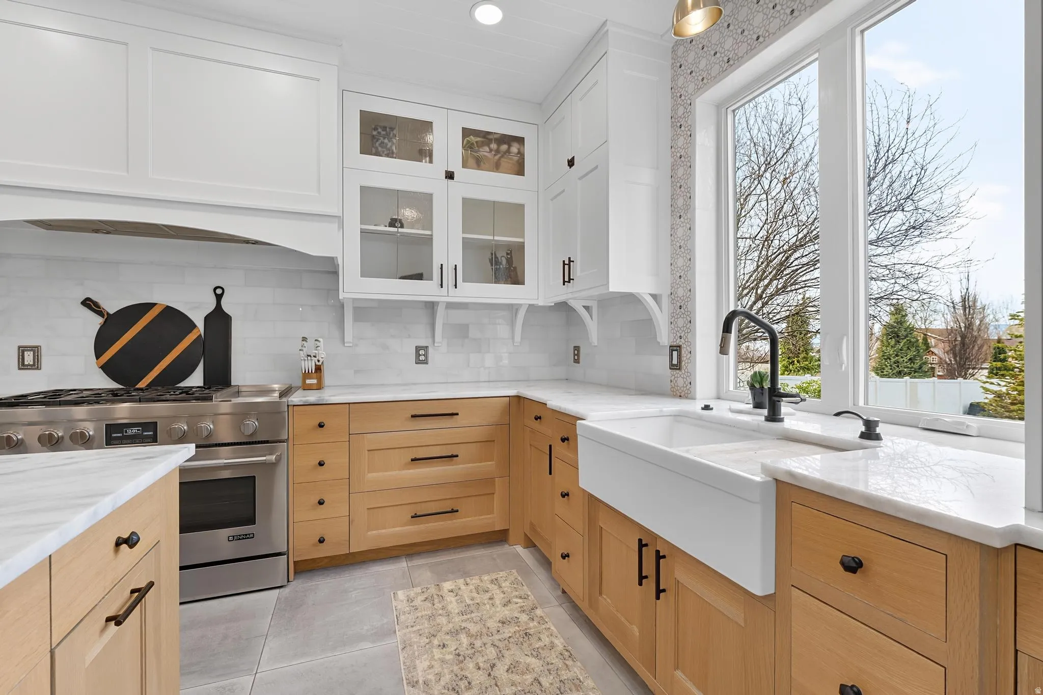 Kitchen with high end range, healthy amount of natural light, light stone counters, glass fronted cabinets, and two tone cabinetry