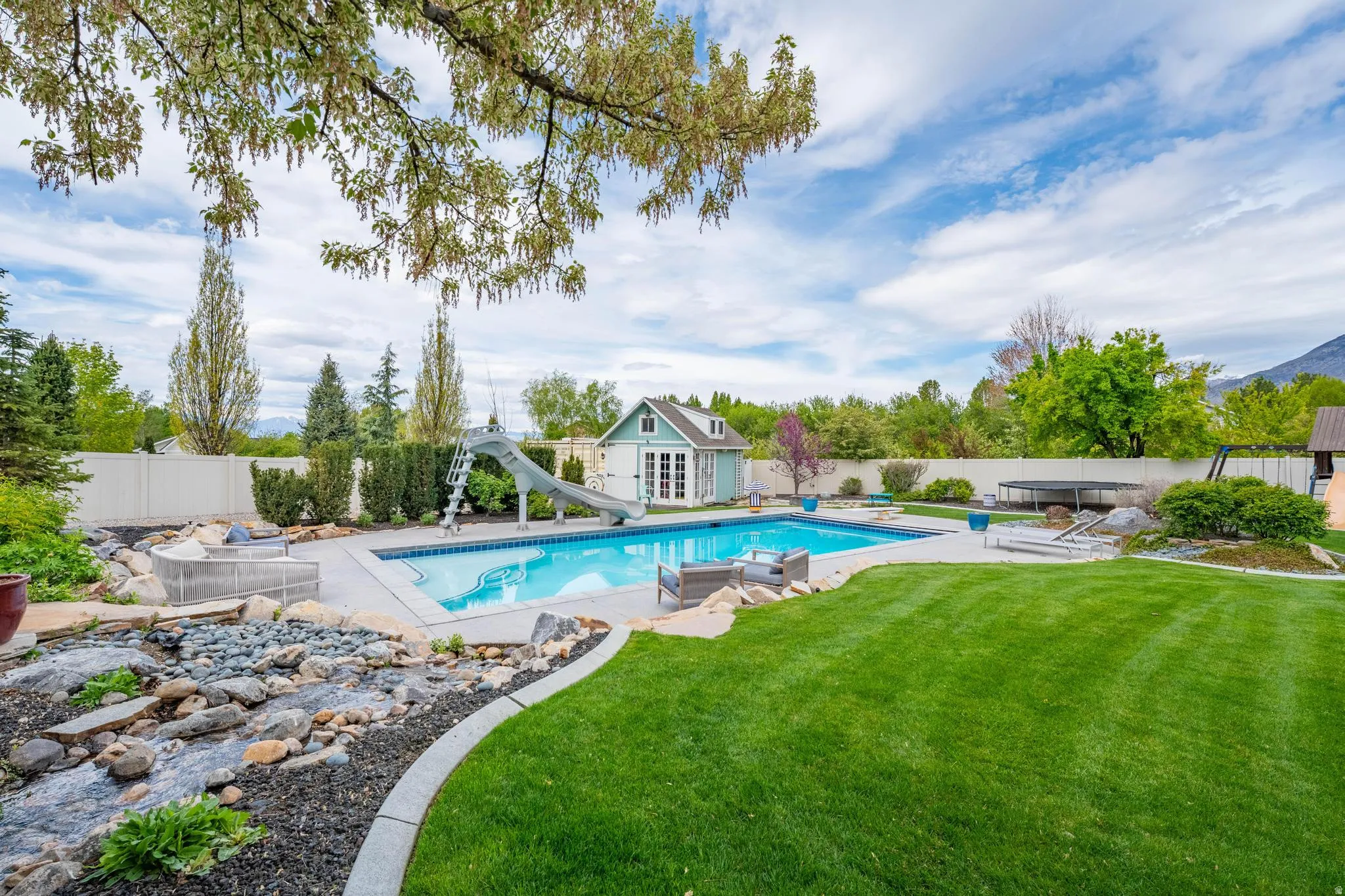 View of pool with an outbuilding, a storage structure, a fenced backyard, a water slide, and patio surround