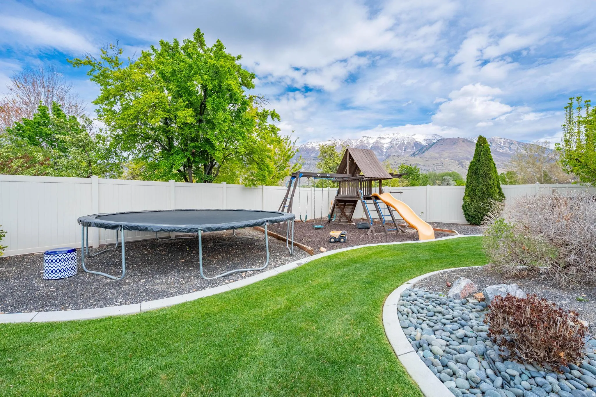 Fenced backyard with a mountain view, a trampoline, and a playground