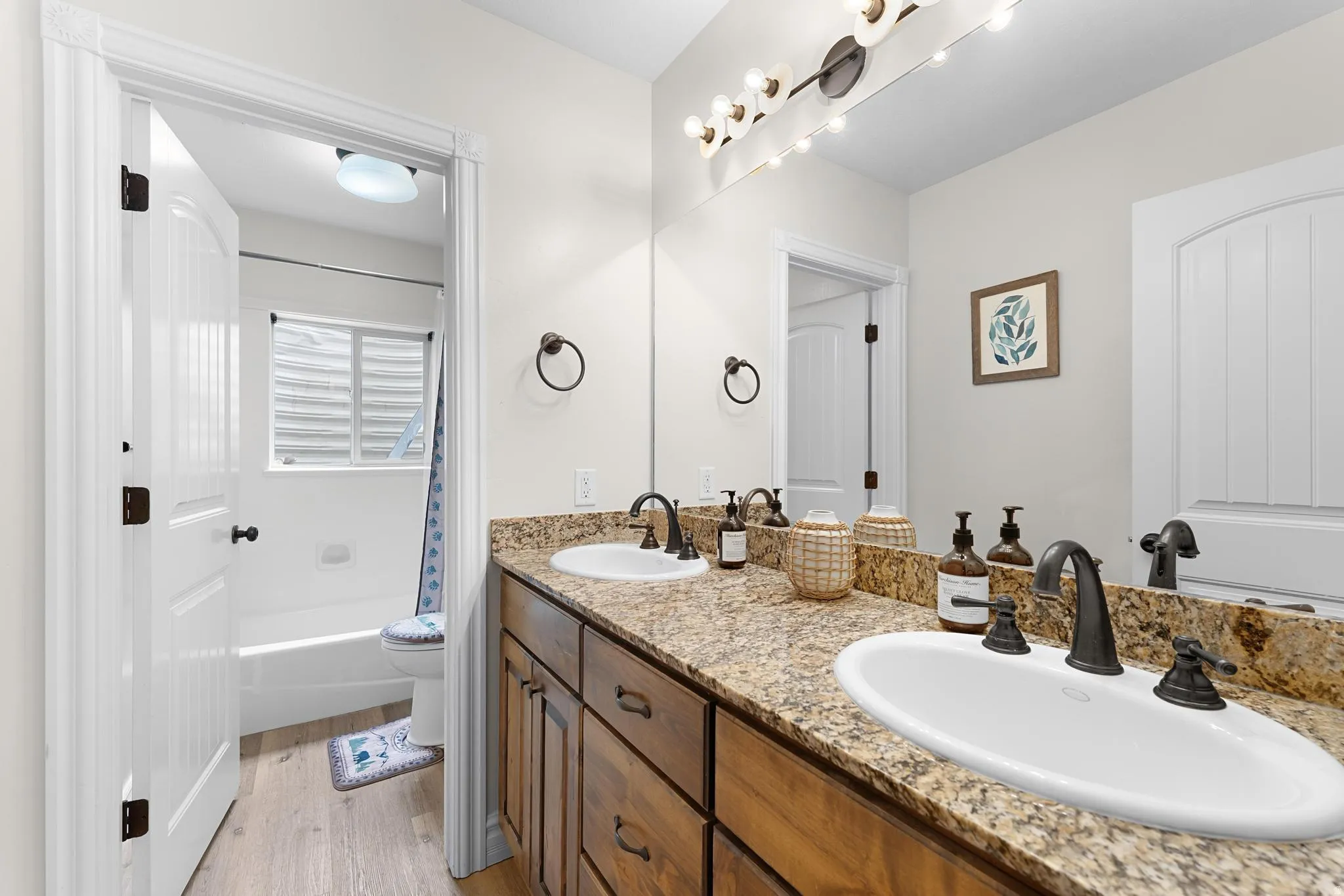 Bathroom featuring double vanity, light wood-style floors, and shower / tub combo