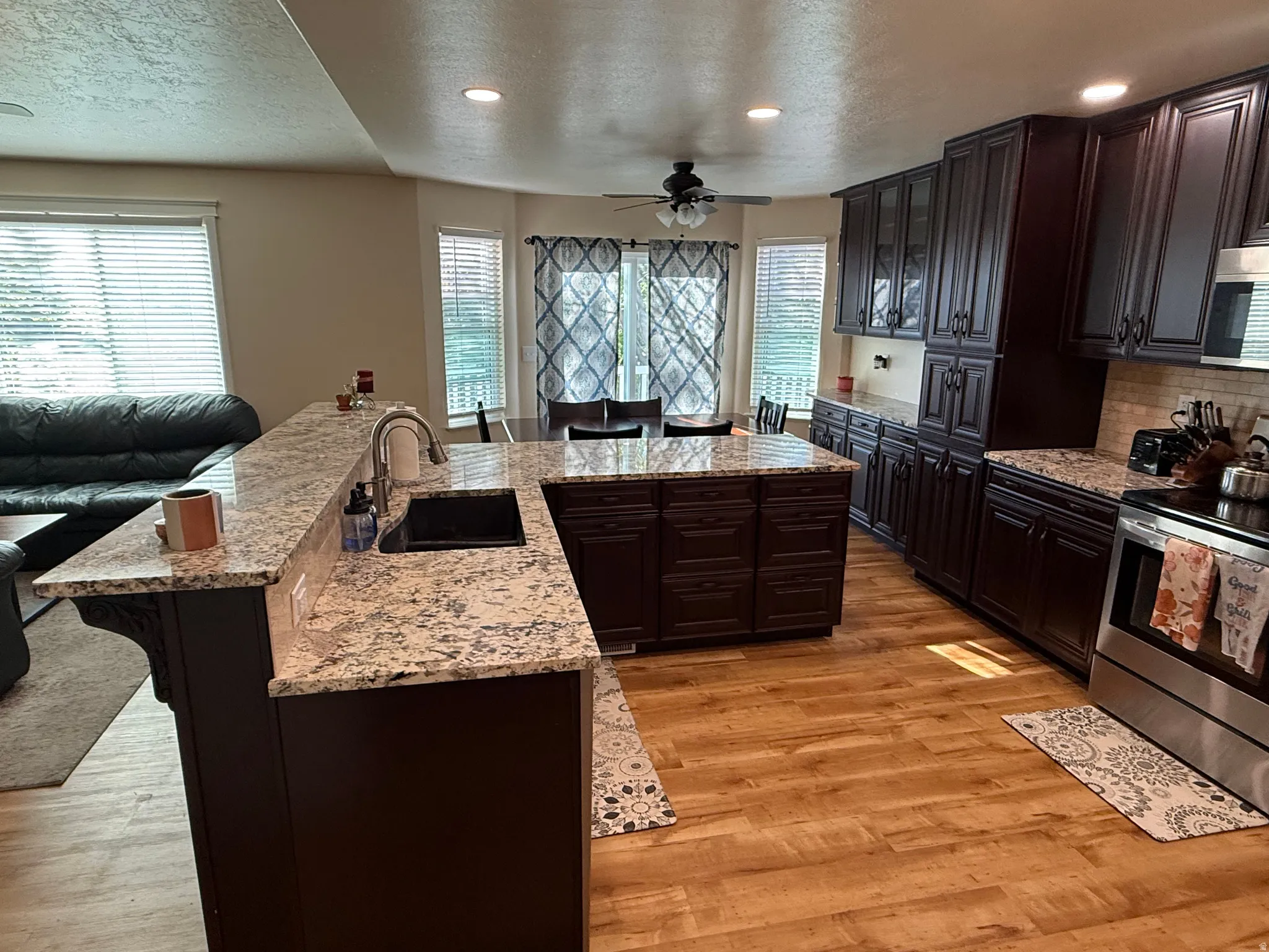 Kitchen featuring a breakfast bar, stainless steel appliances, dark wood finish cabinetry, light stone counters, and recessed lighting
