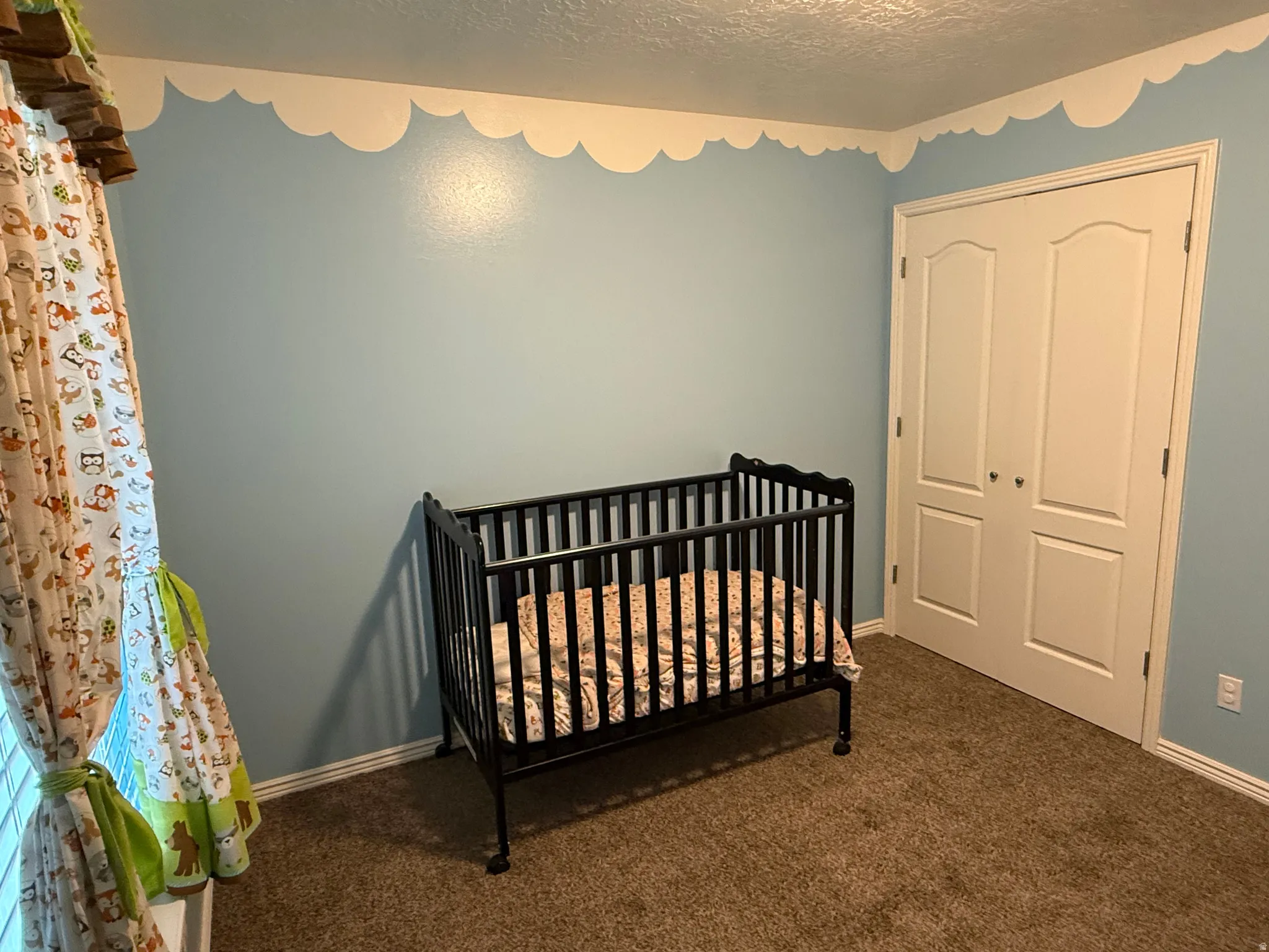 Carpeted bedroom featuring a nursery area, a closet, and a textured ceiling
