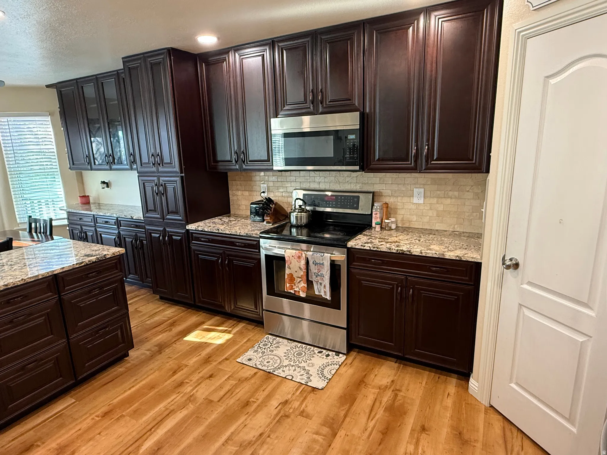 Kitchen featuring stainless steel appliances, dark wood finish cabinets, glass insert cabinets, light stone countertops, and a textured ceiling