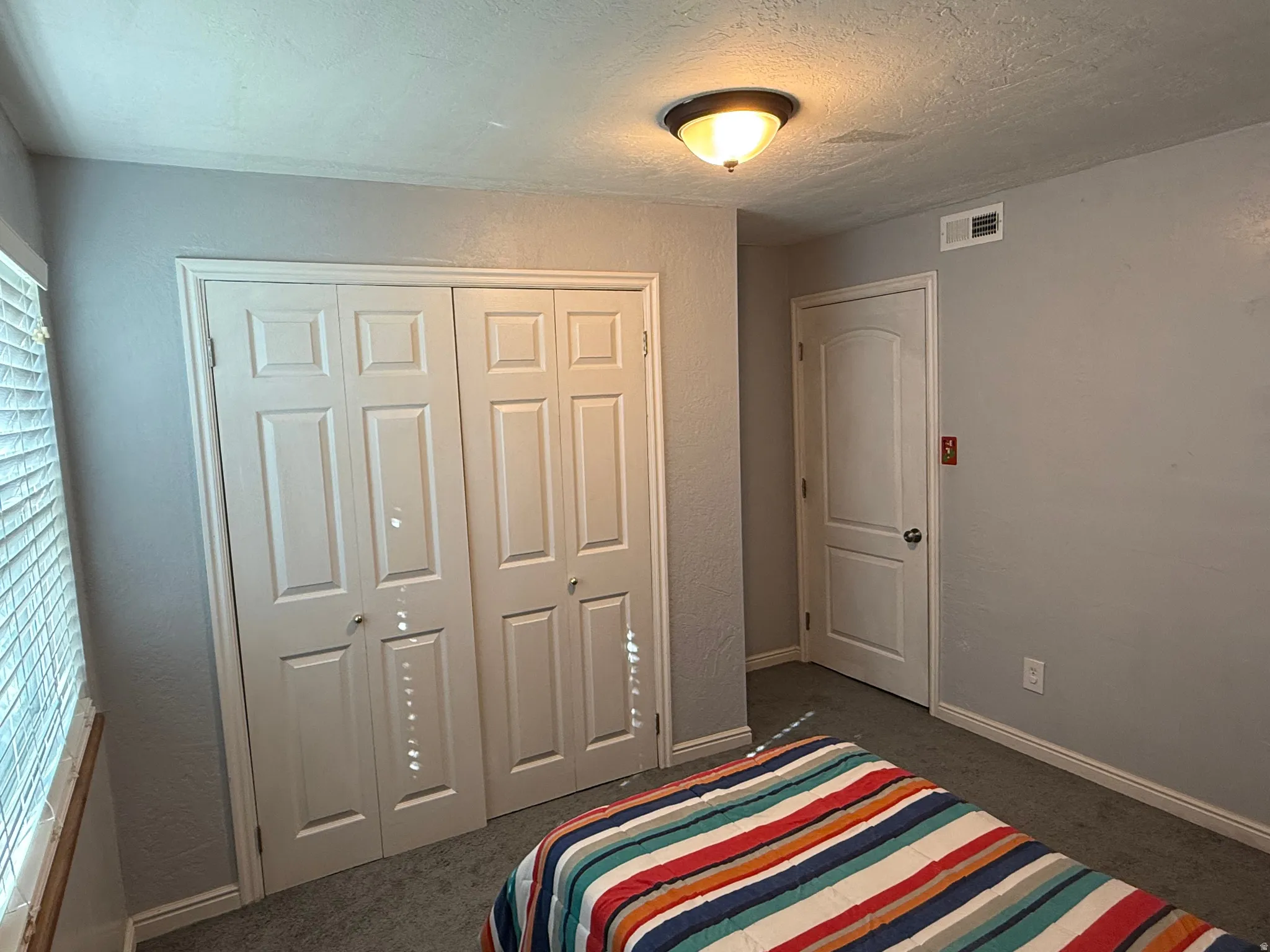 Bedroom featuring a textured ceiling, dark colored carpet, a textured wall, and a closet