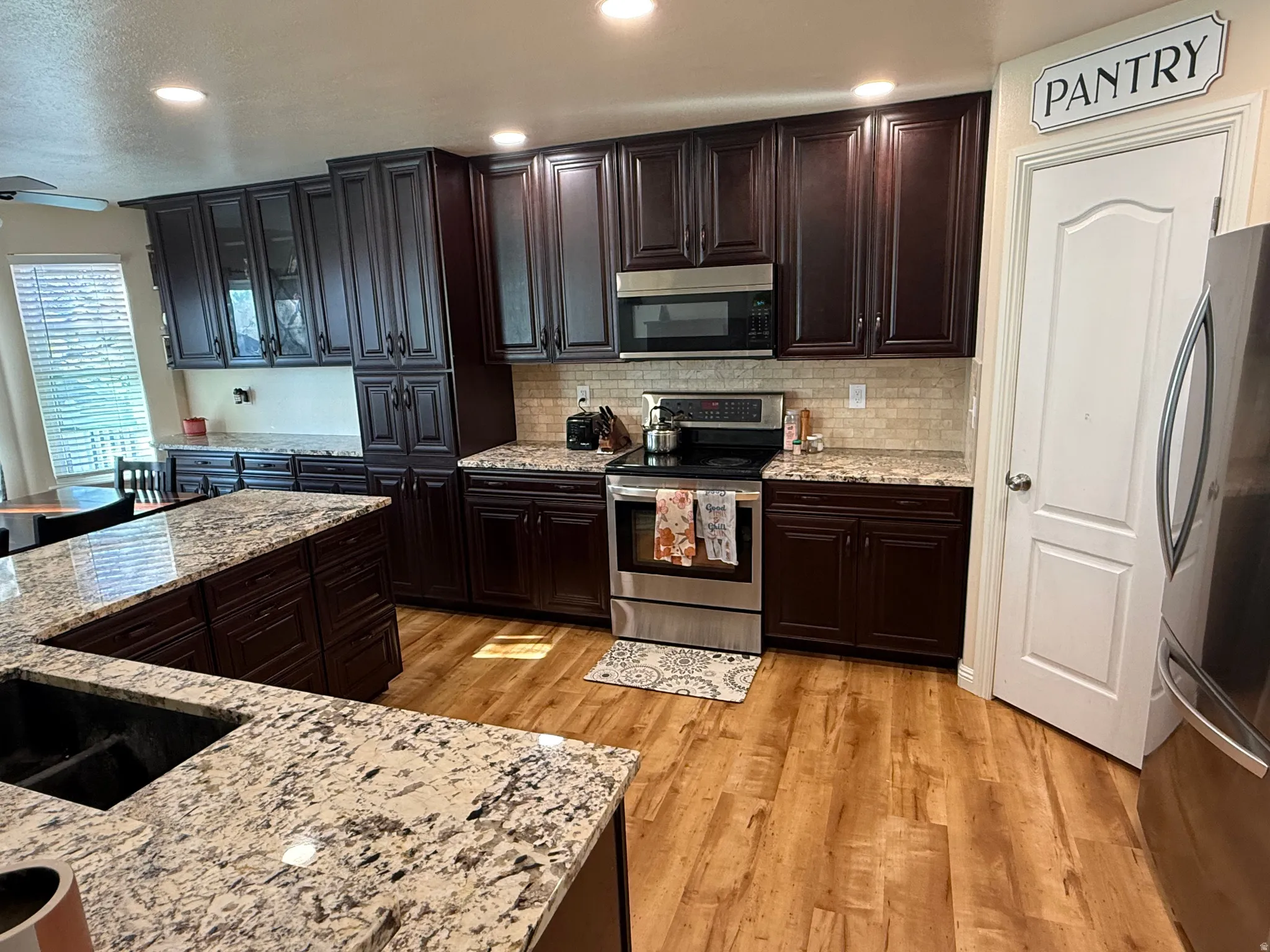 Kitchen with stainless steel appliances, recessed lighting, light wood-type flooring, dark wood finish cabinetry, and glass insert cabinets