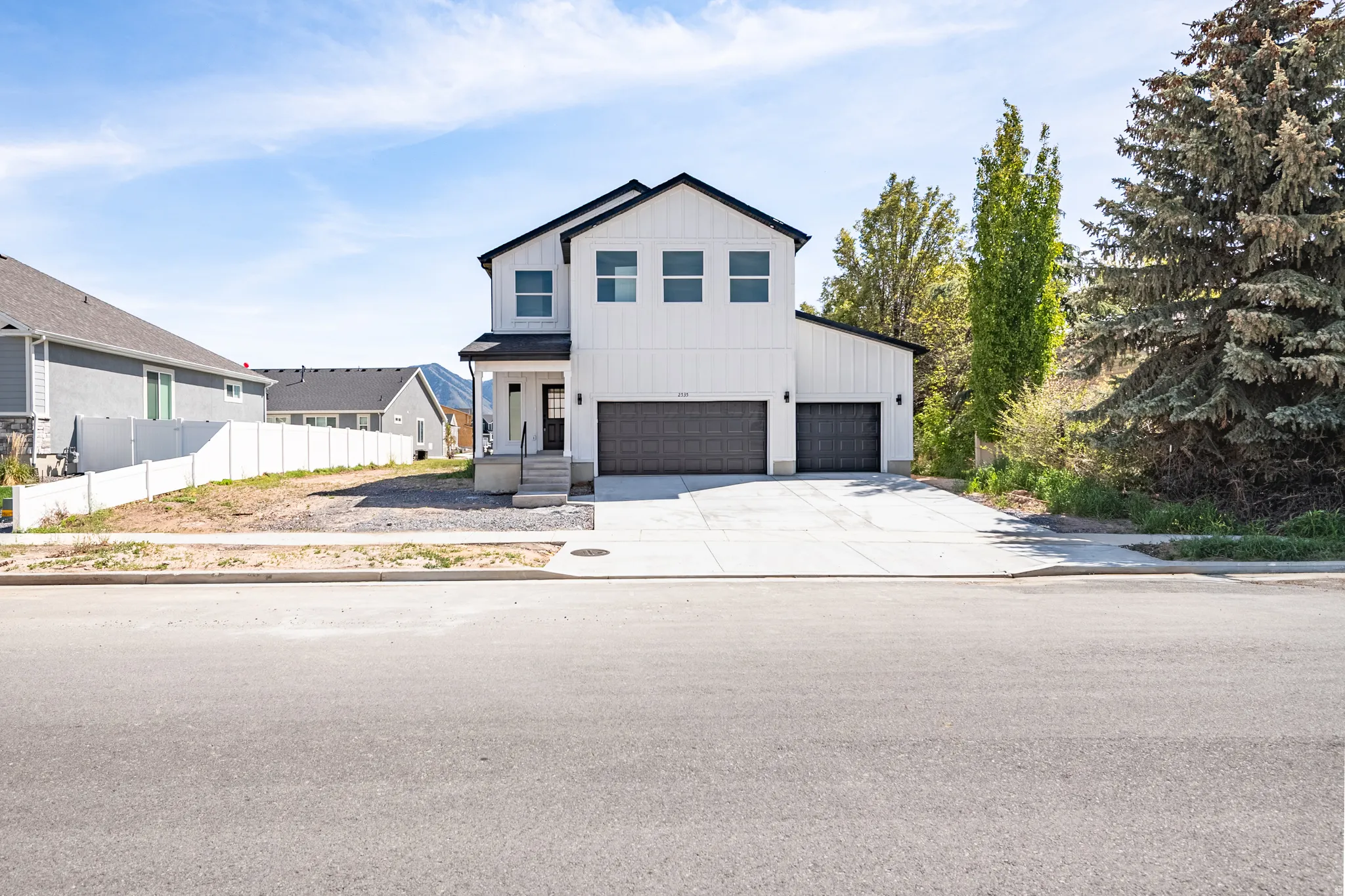 Modern farmhouse exterior featuring white vertical siding, black-framed windows, a covered entry, and two dark garage doors