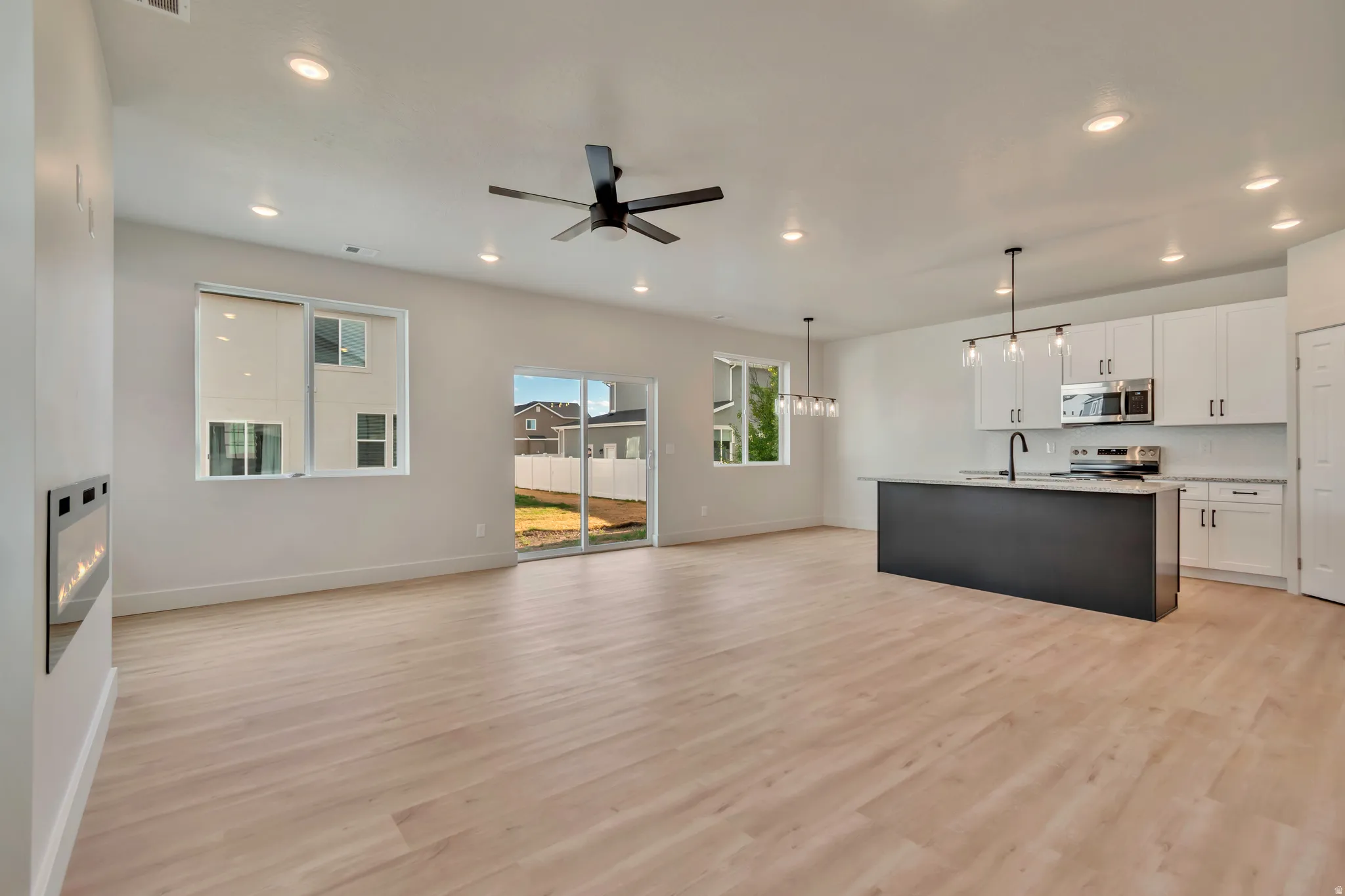 Unfurnished living room featuring ceiling fan, light wood-type flooring, a glass covered fireplace, and hanging lights