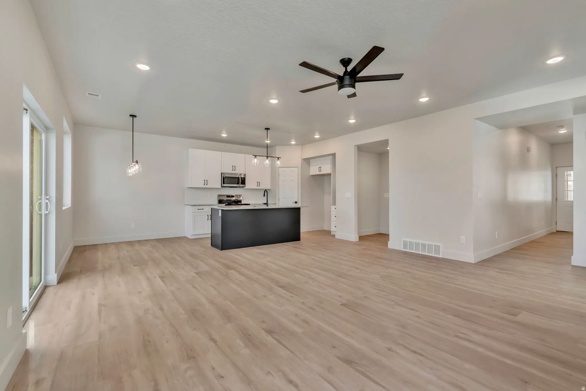 Two tone kitchen with open floor plan, light wood-style flooring, a ceiling fan, decorative light fixtures, and a center island with sink