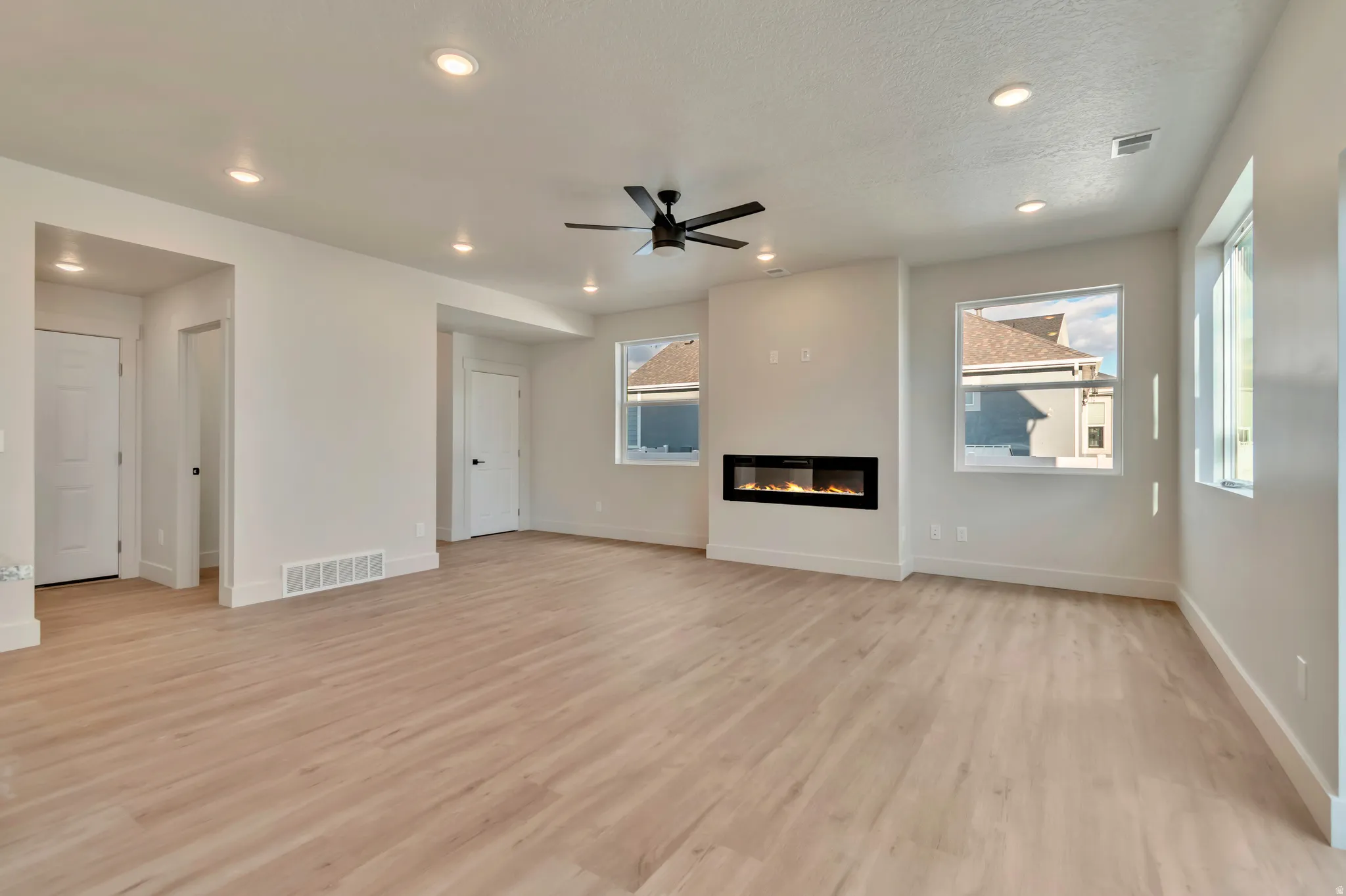 Unfurnished living room featuring a glass covered fireplace, ceiling fan, light wood-style flooring, and recessed lighting