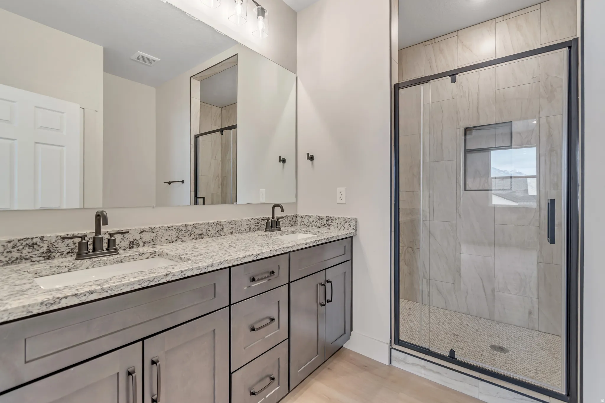 Bathroom featuring double vanity, a stall shower, and light wood-style flooring