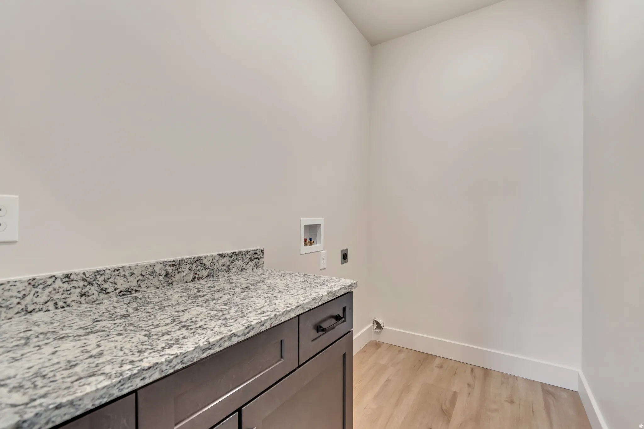 Laundry area with light wood-type flooring, hookup for an electric dryer, washer hookup, and cabinet space
