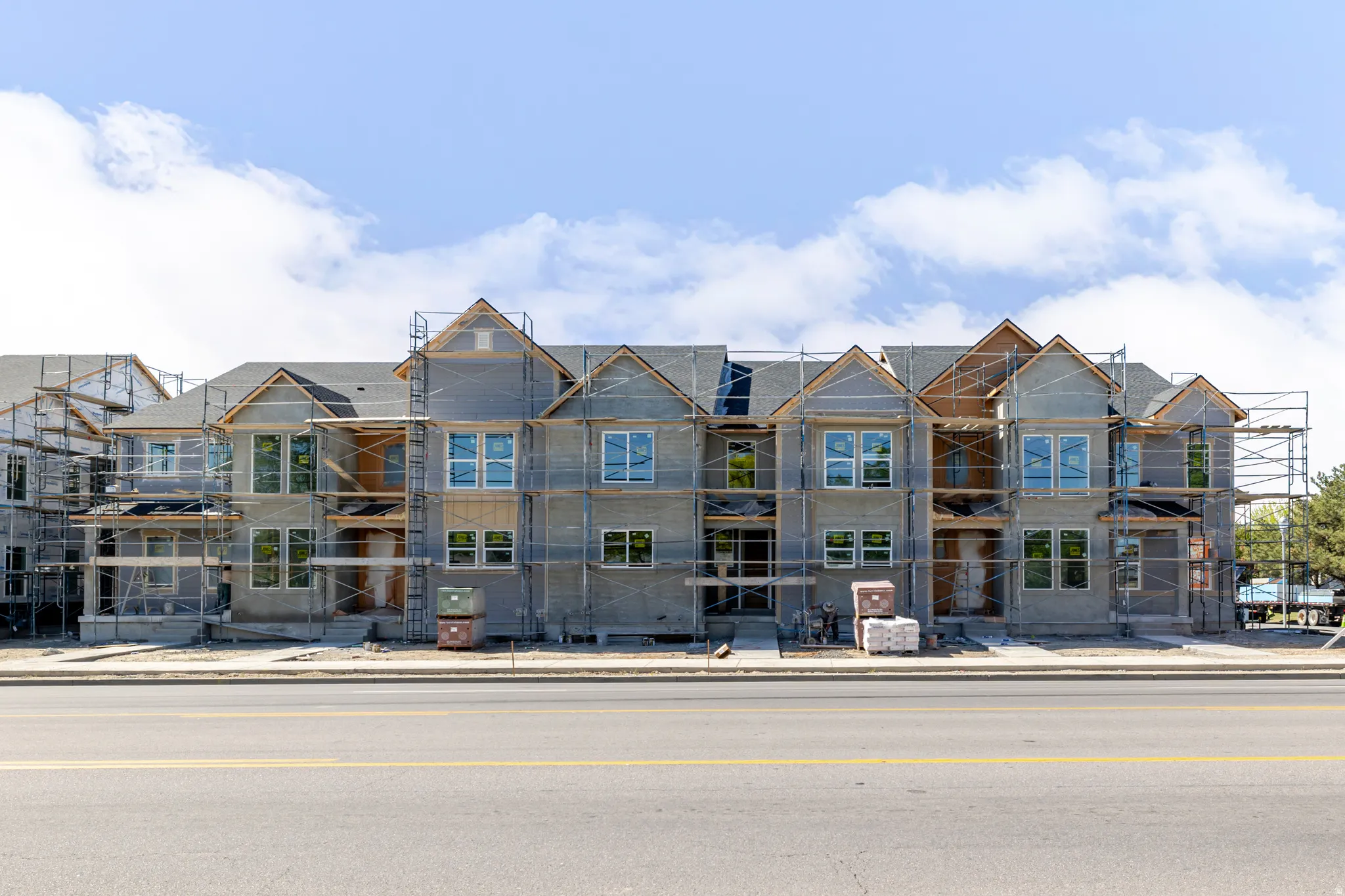 New construction townhome development featuring multiple gabled rooflines, dark shingle roofing, and numerous windows