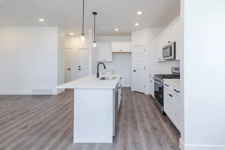 Contemporary kitchen featuring white cabinetry, a large center island with integrated sink, stainless steel appliances, and wood-finish flooring