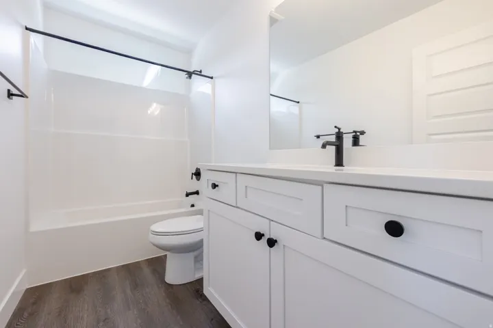 White shaker cabinetry with black hardware, complementing black plumbing fixtures, solid surface countertop, and wood-finish flooring