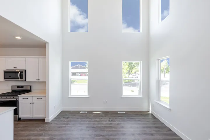 Vaulted ceilings, a kitchen with white cabinetry and stainless steel appliances, and wood-finish flooring