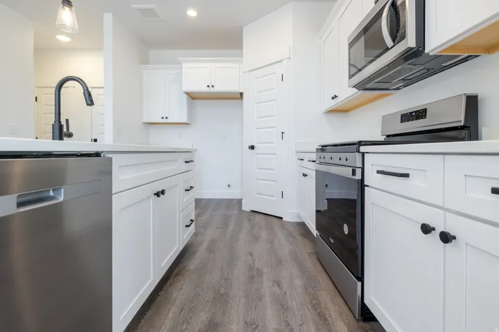 Contemporary kitchen featuring white cabinetry, stainless steel appliances, wood-finish flooring, and a matte black faucet