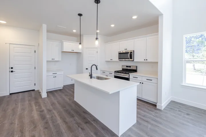 Kitchen featuring an island with an undermount sink, white cabinetry, stainless steel appliances, and wood-finish flooring