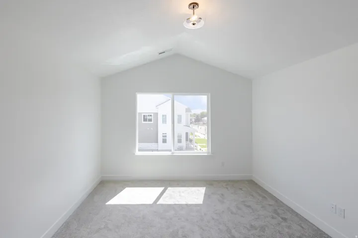 Vaulted ceiling room with neutral carpeting and a single window